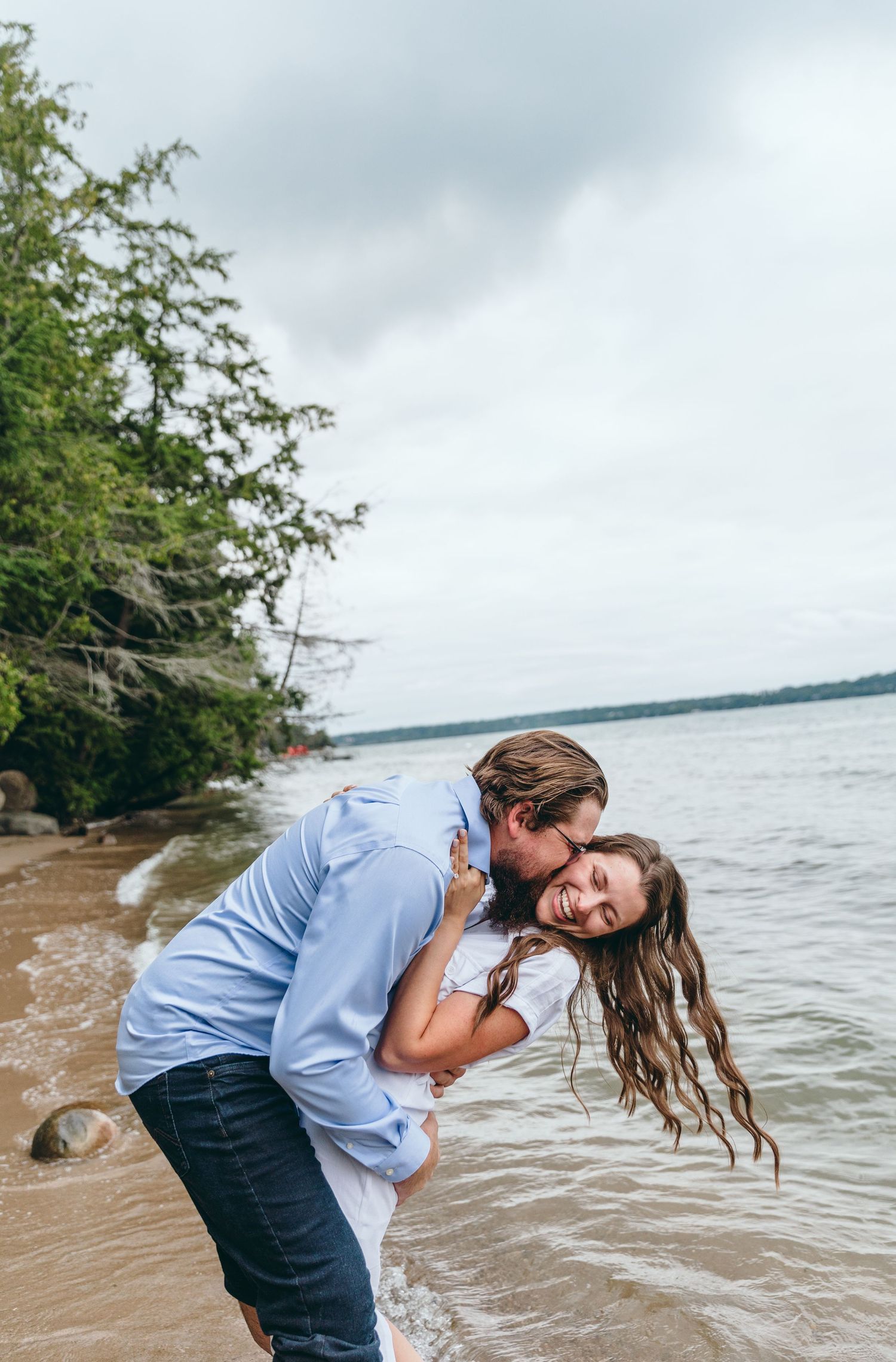 A playful romantic moment captured on a rocky beach with waves and cloudy skies in the background.