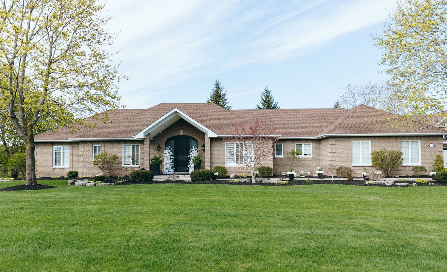 Large ranch-style home with brown exterior and covered entry porch on expansive green lawn.