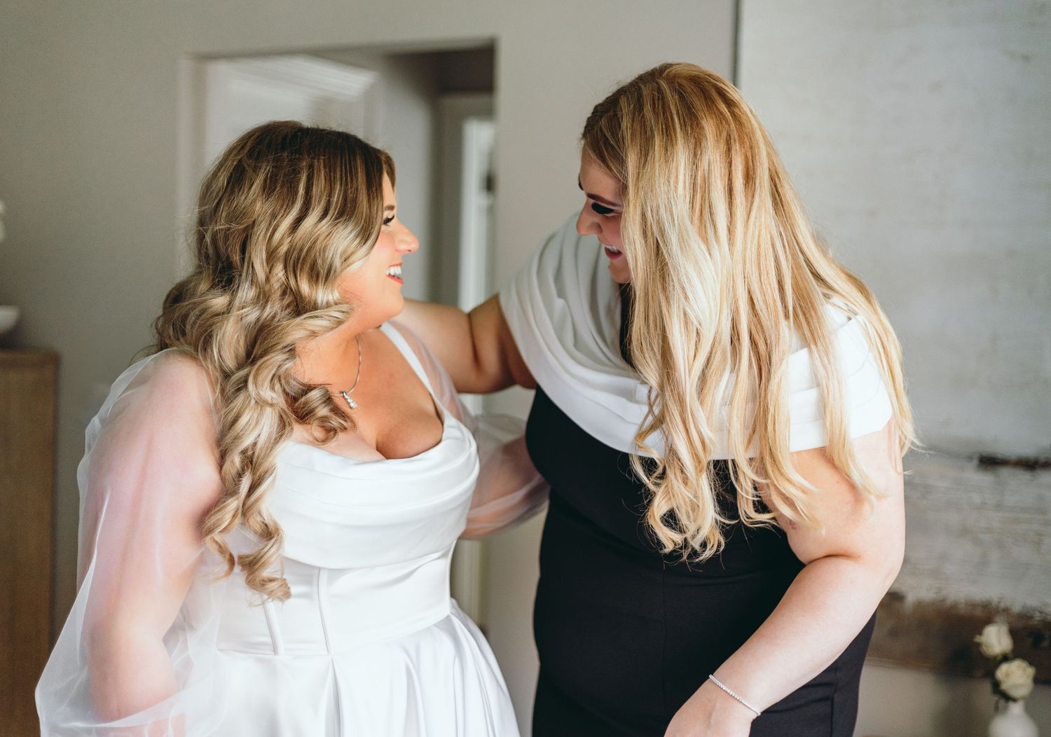 Wedding party members help with final dress adjustments in a bright indoor setting.