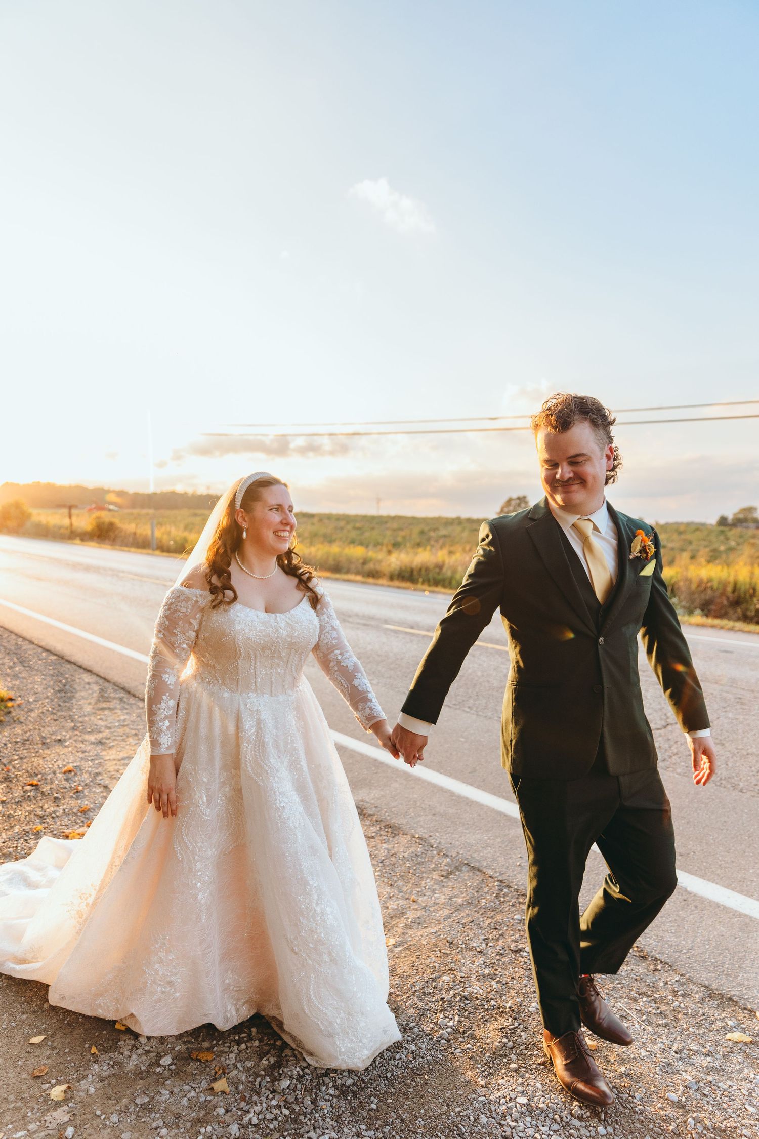 Playful wedding couple running along a desert road at sunset.