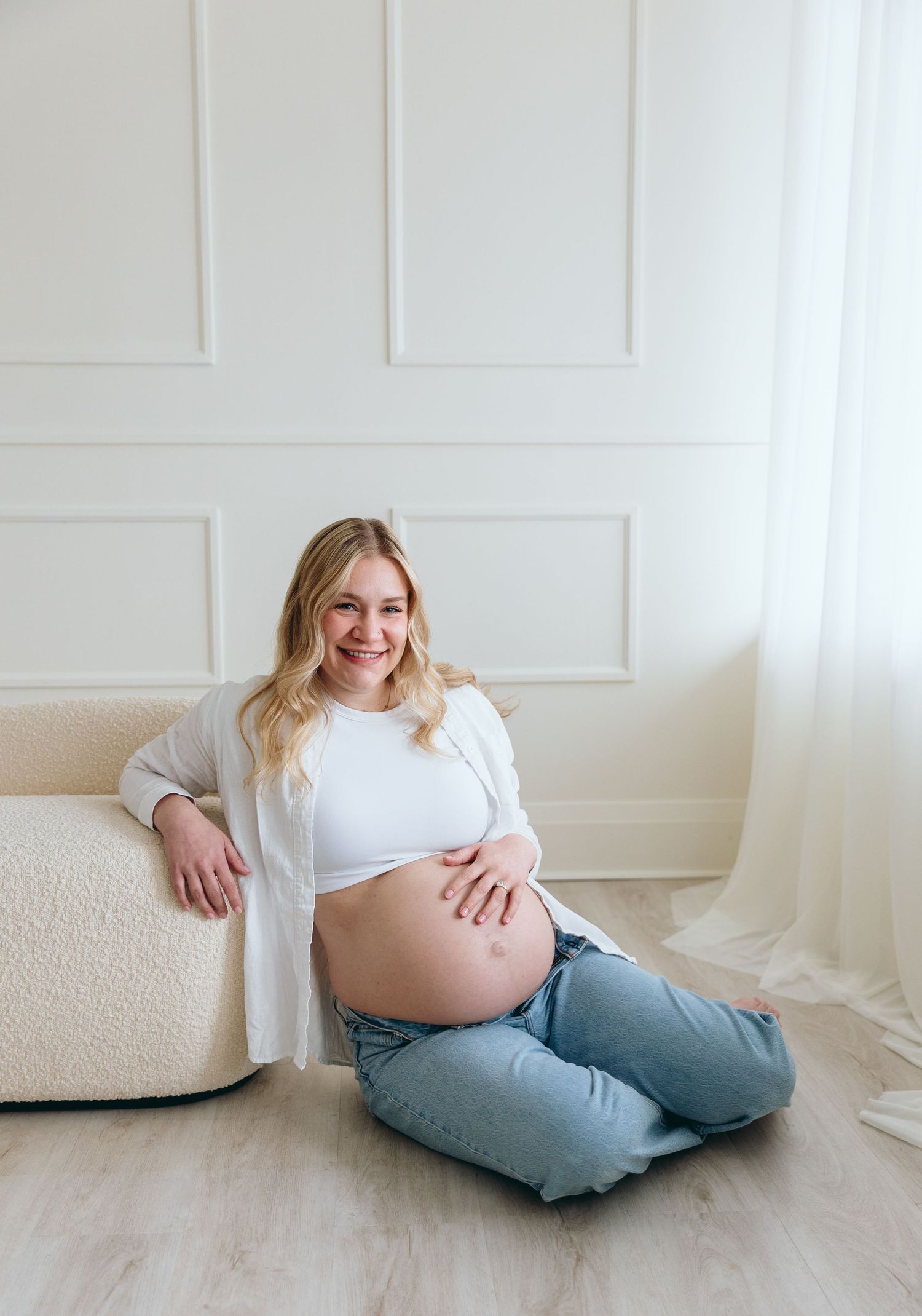 Casual maternity portrait of expectant mother relaxing on floor in jeans and white top.