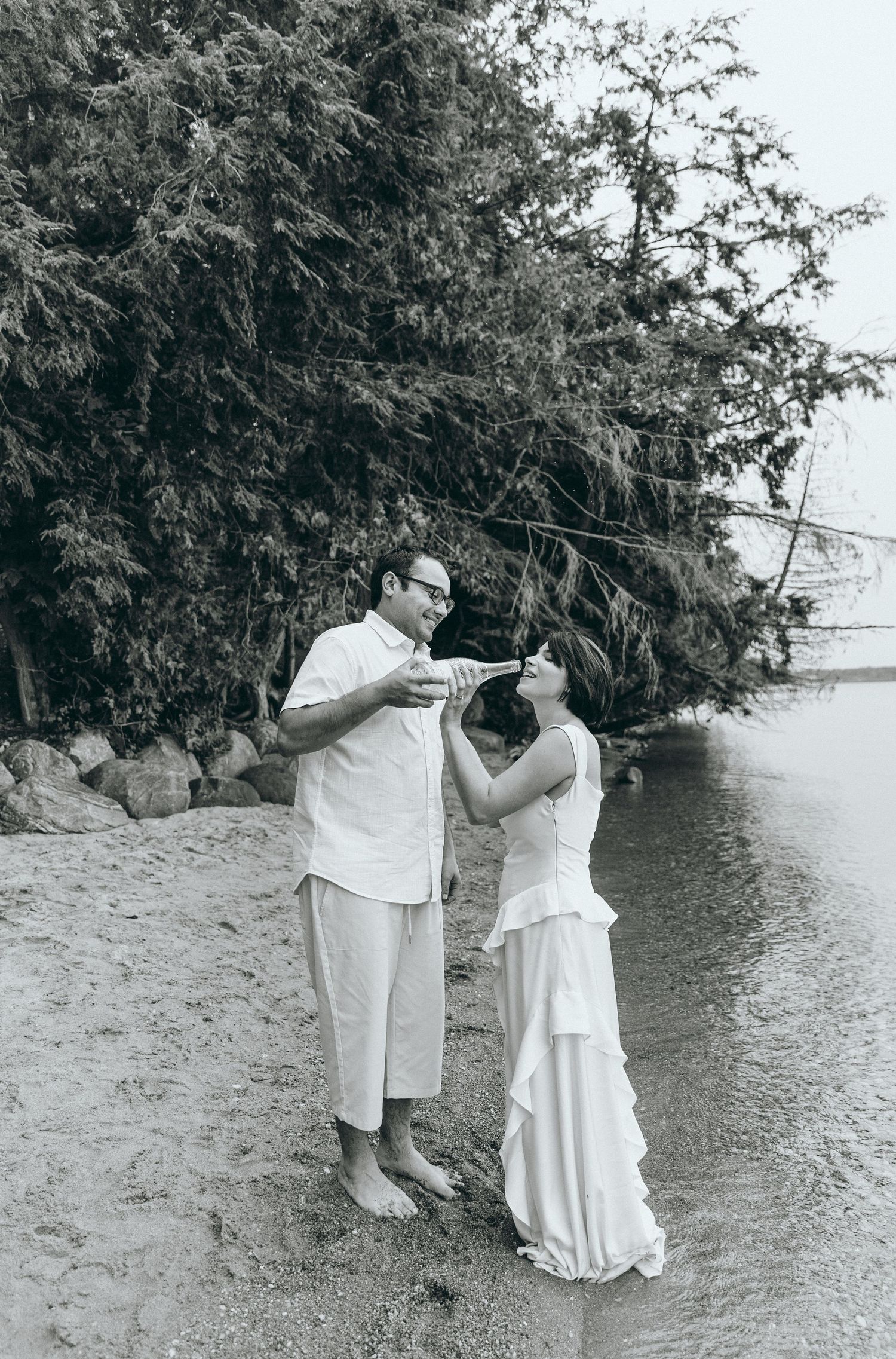 Romantic couple photoshoot by the water's edge with trees in the background.