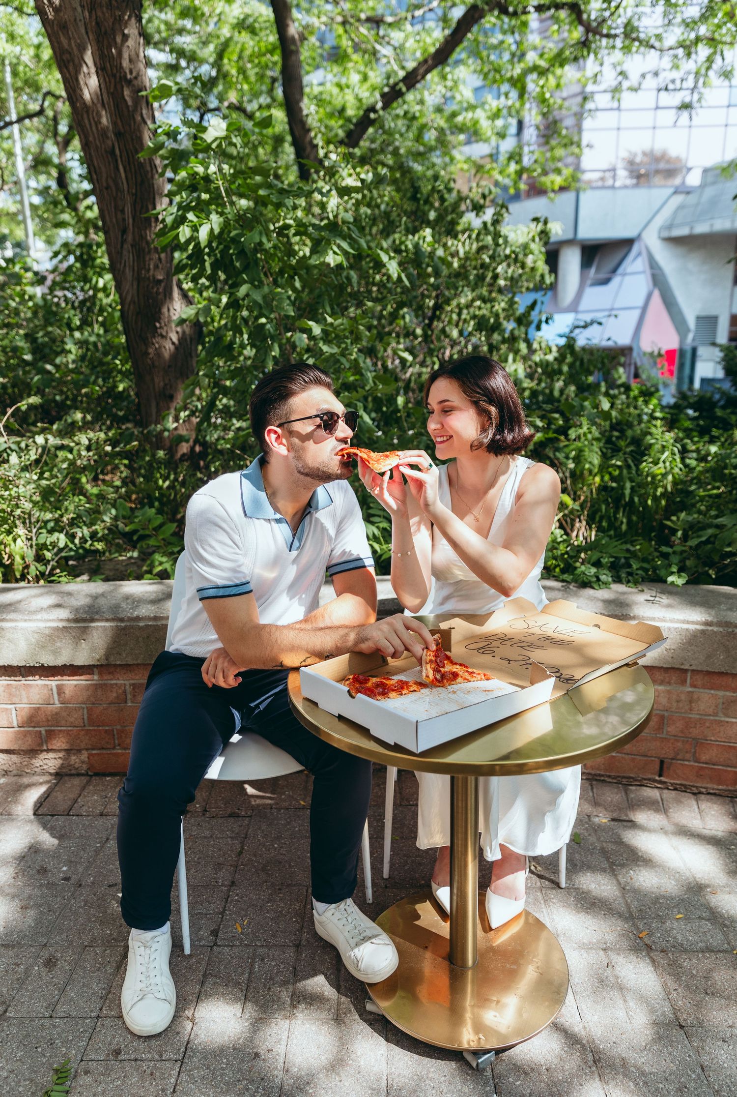 Two people share pizza while dining at an outdoor cafe table.