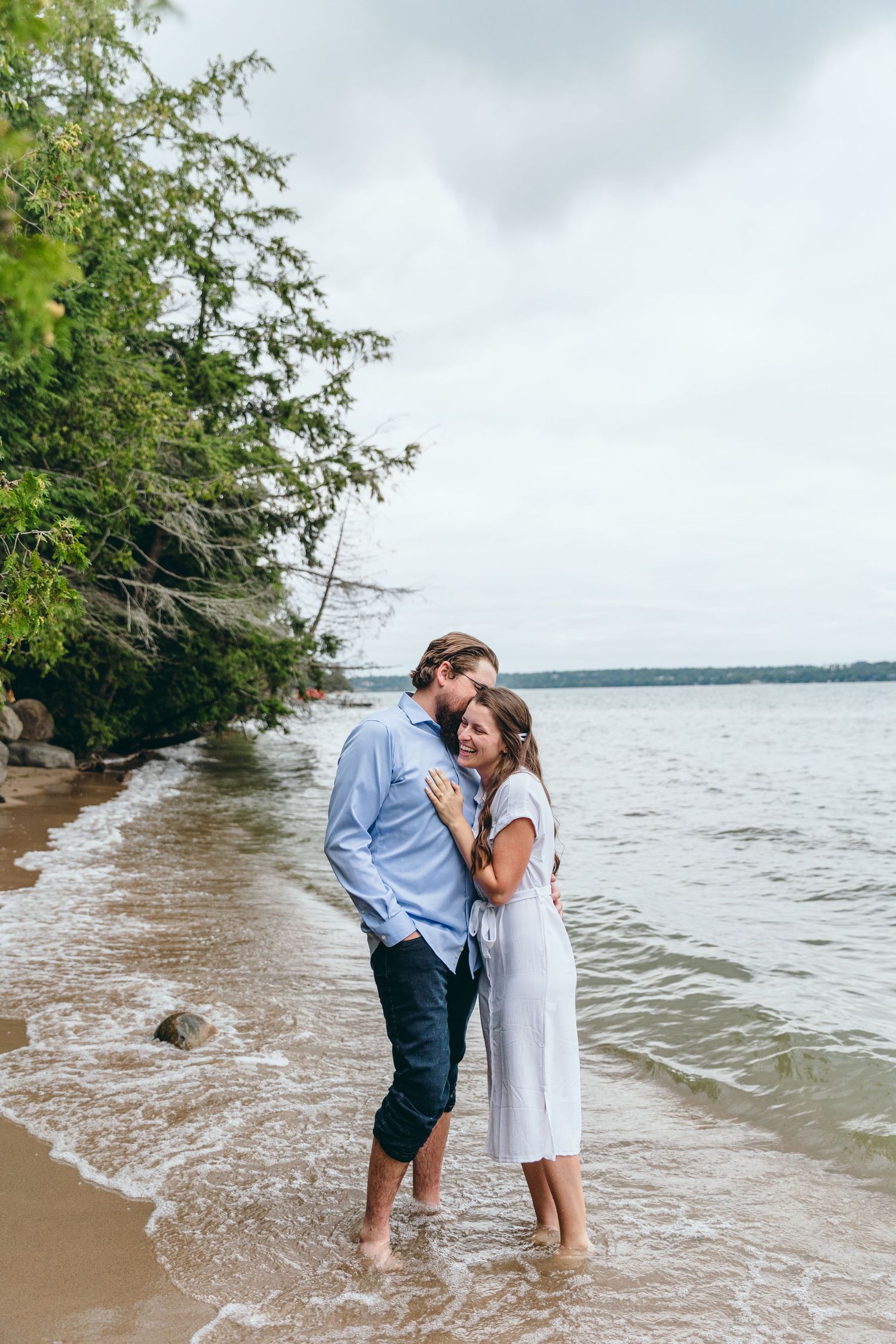 Two people share intimate moment while standing in shallow water at lakeside beach.