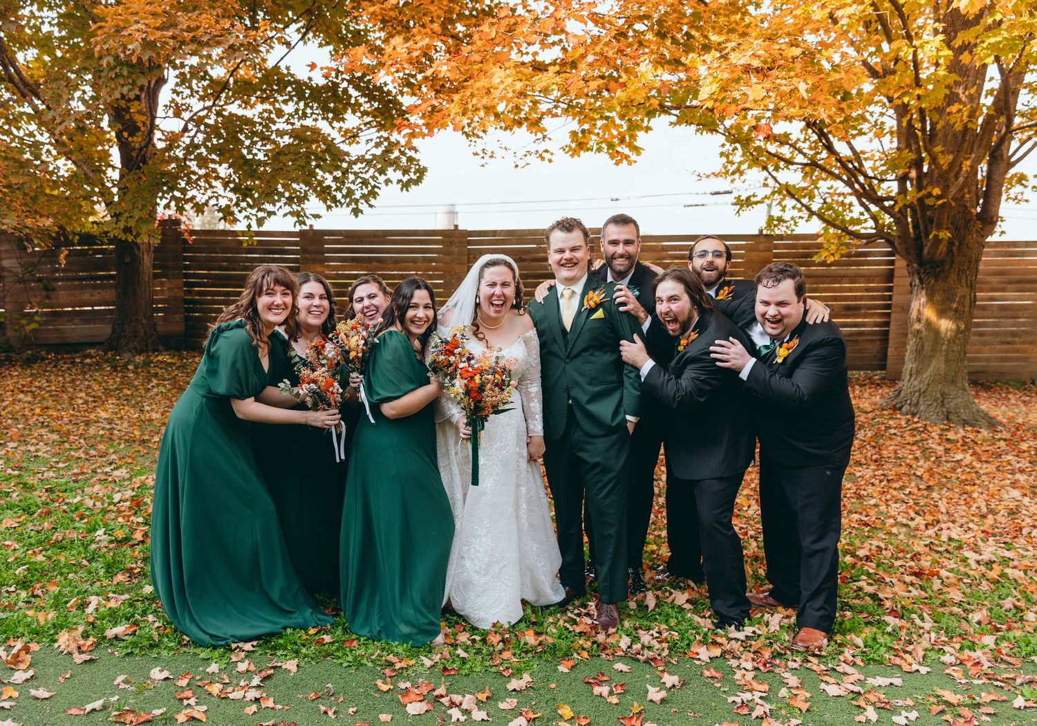 Bridal party takes fun group photos under orange autumn trees.