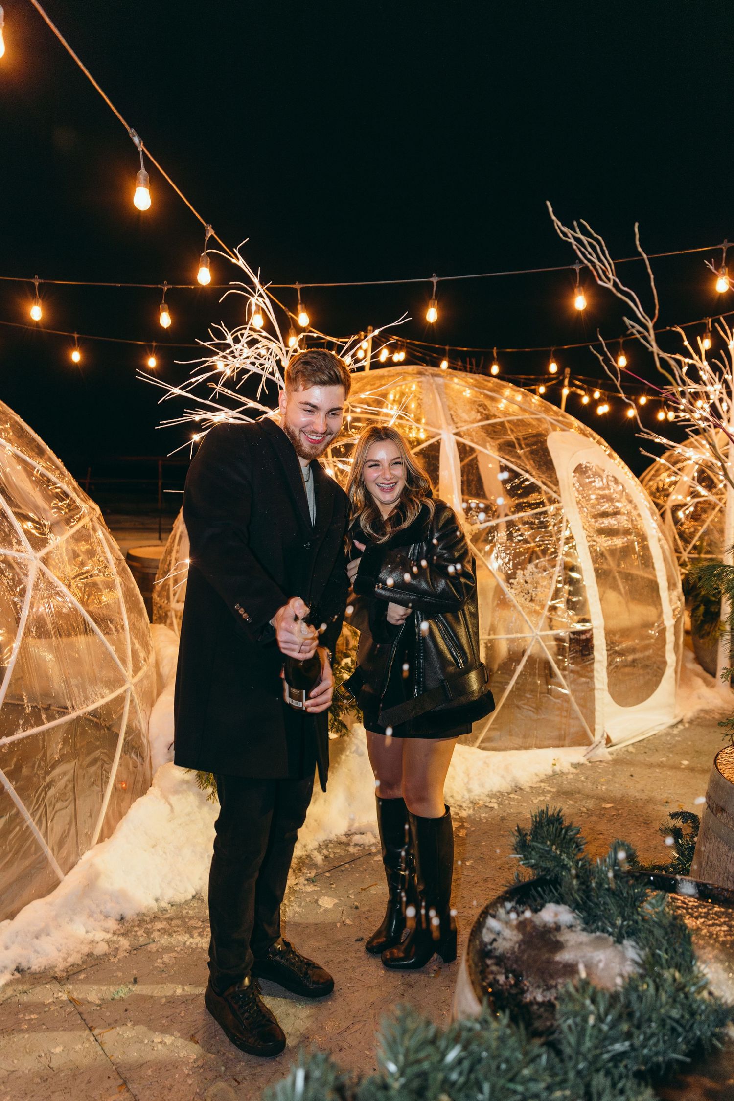 Couple celebrating with sparklers against illuminated letters and string lights.