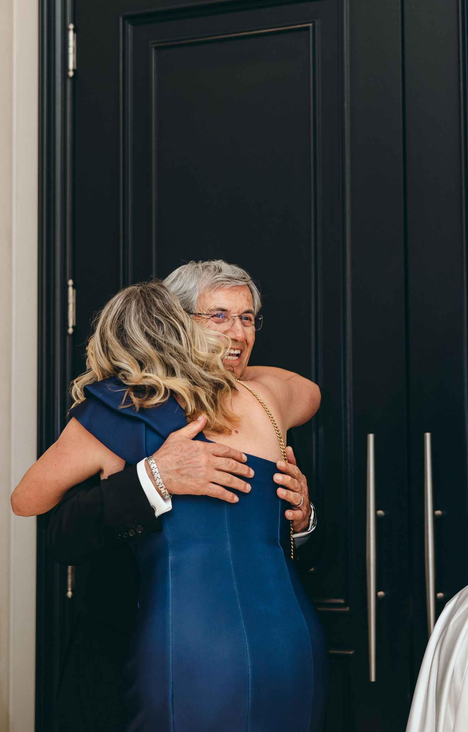 Emotional embrace at formal event with navy blue dress against dark door.