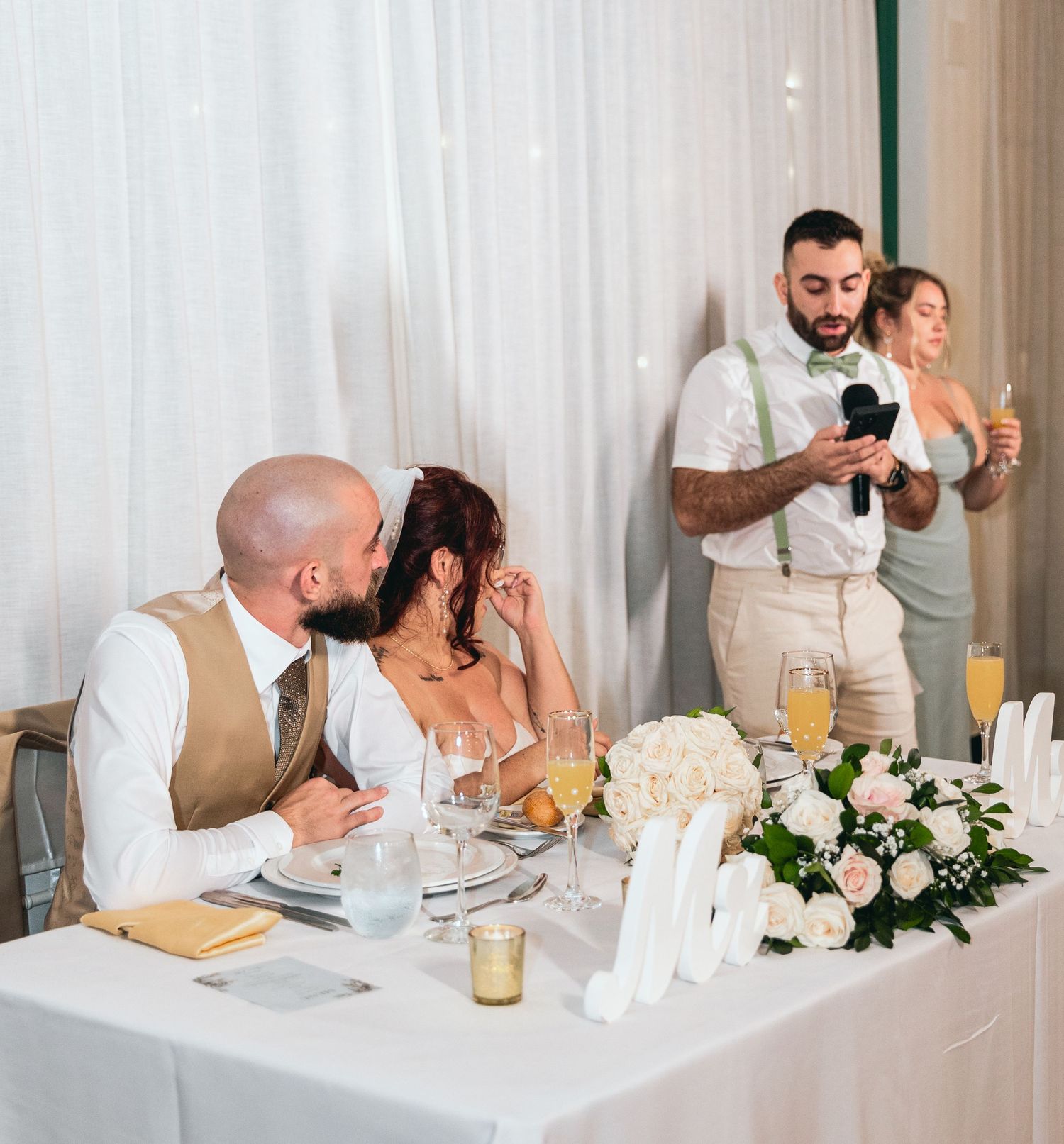 Wedding party seated at head table with white floral centerpieces during reception.