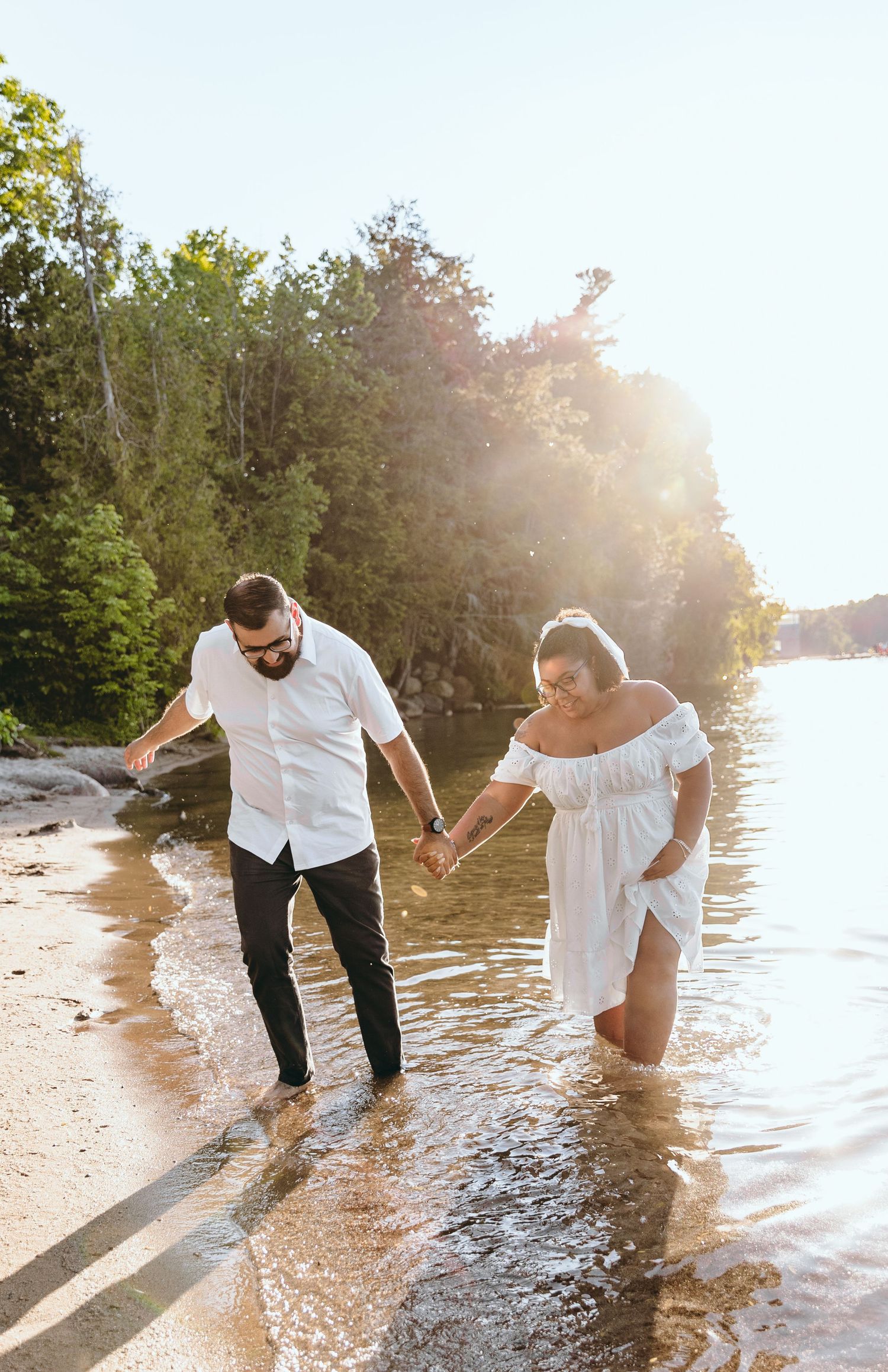 A couple plays and splashes in the water at sunset along a beach shoreline.