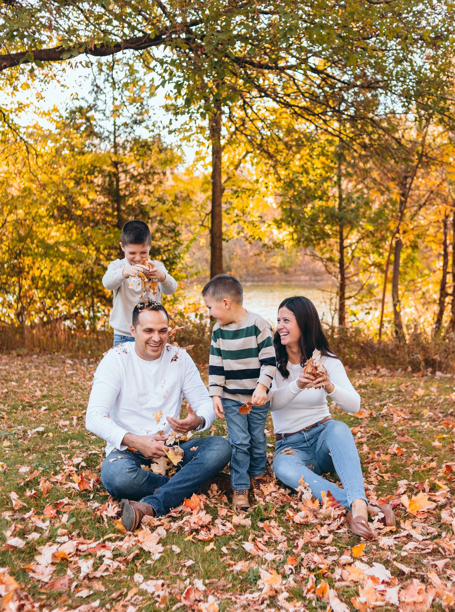 Family enjoying a casual fall photoshoot on ground covered with autumn leaves.