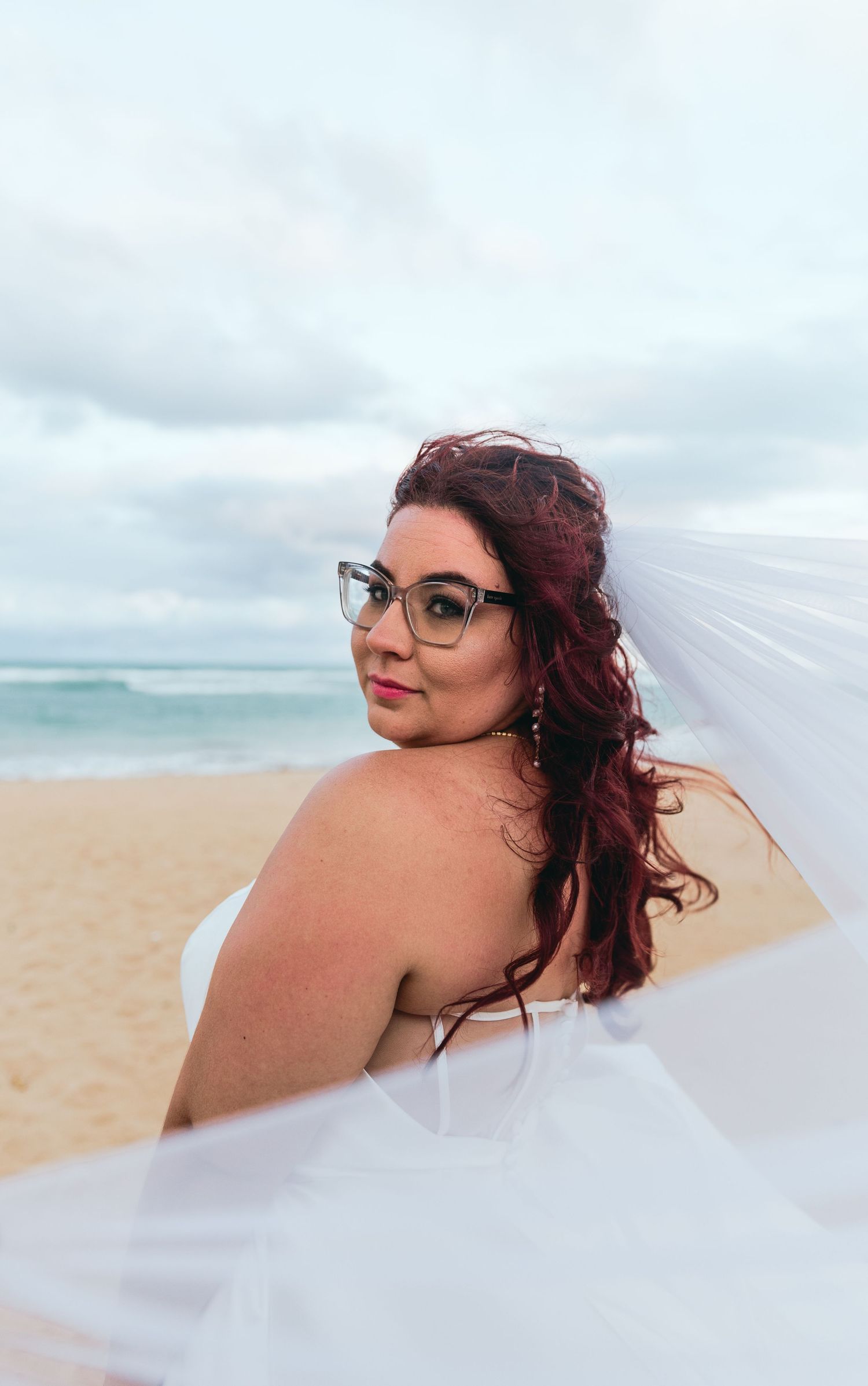 Flowing white veil catches the ocean breeze during beach wedding portraits.