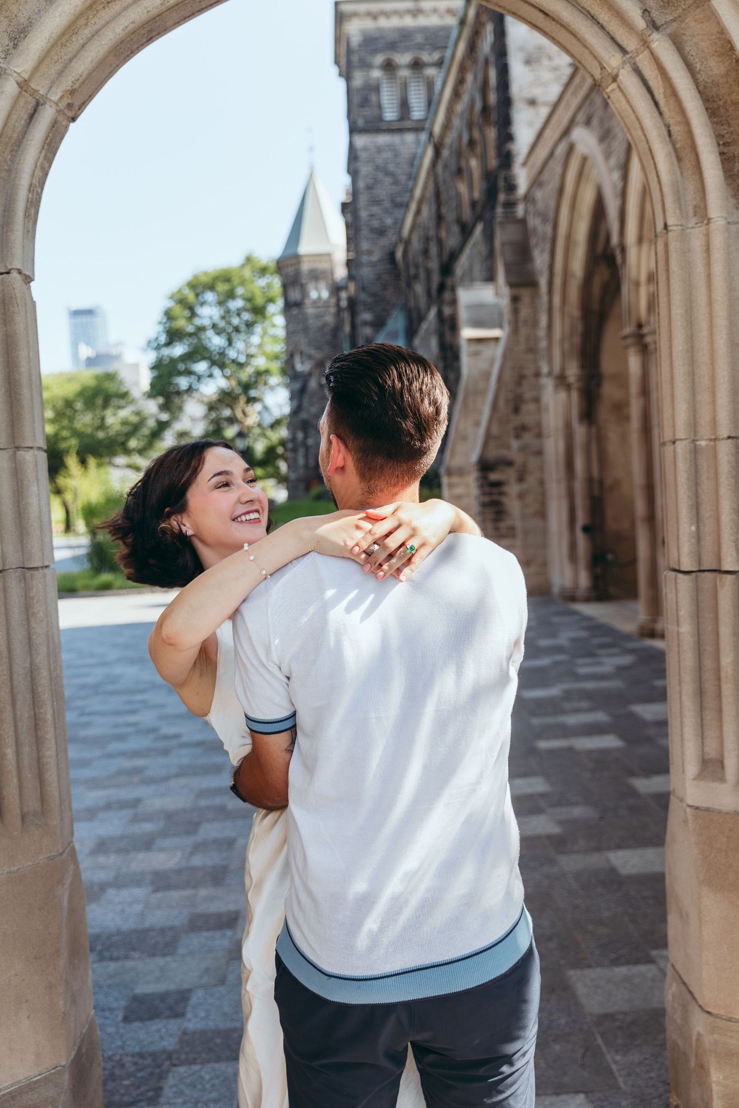 A couple shares a romantic moment under a gothic stone archway on a sunny day.