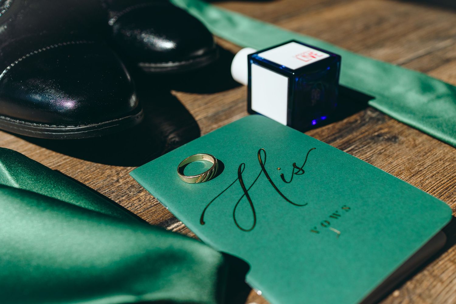 Green stationery and wedding details arranged on dark wooden surface.