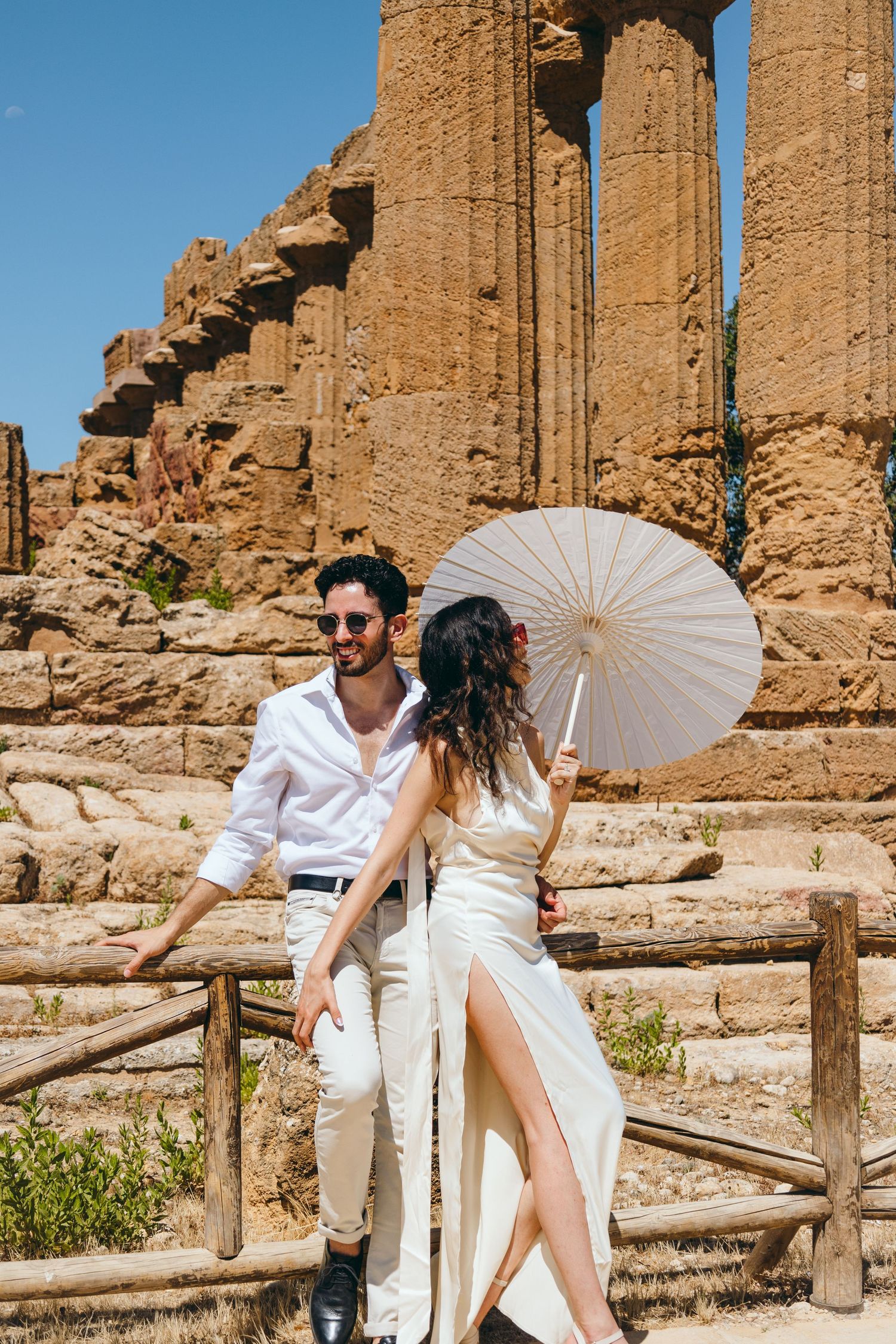 Stylish couple with white parasol share romantic moments at historic temple site.