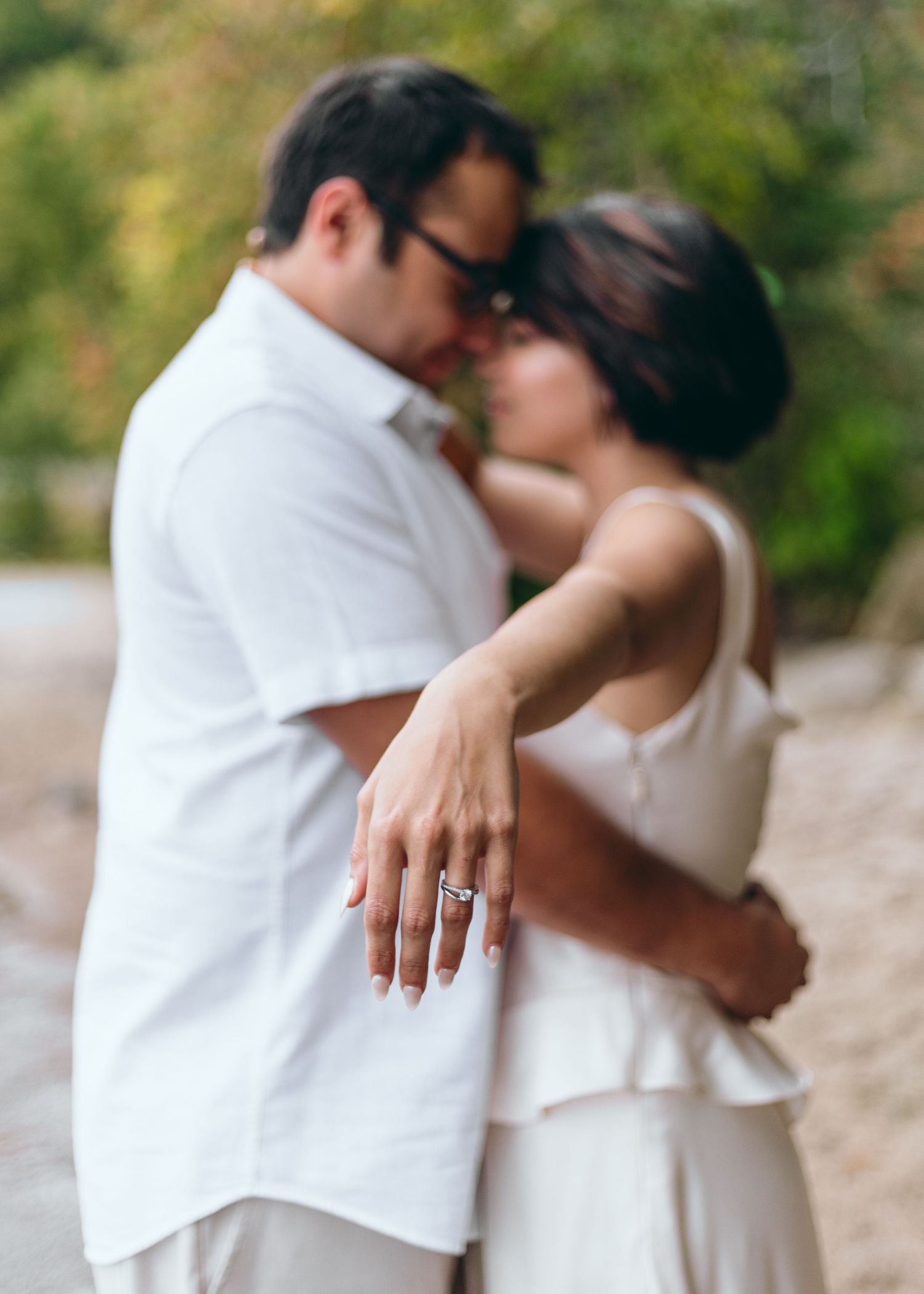 Couple embracing on beach while showing off engagement ring.