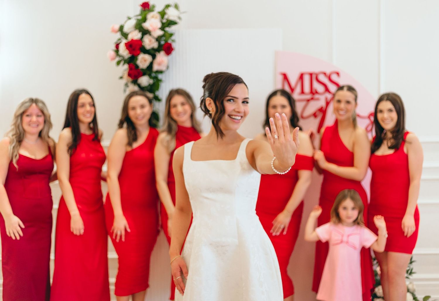 Bridesmaids in matching red dresses pose together at a wedding celebration.