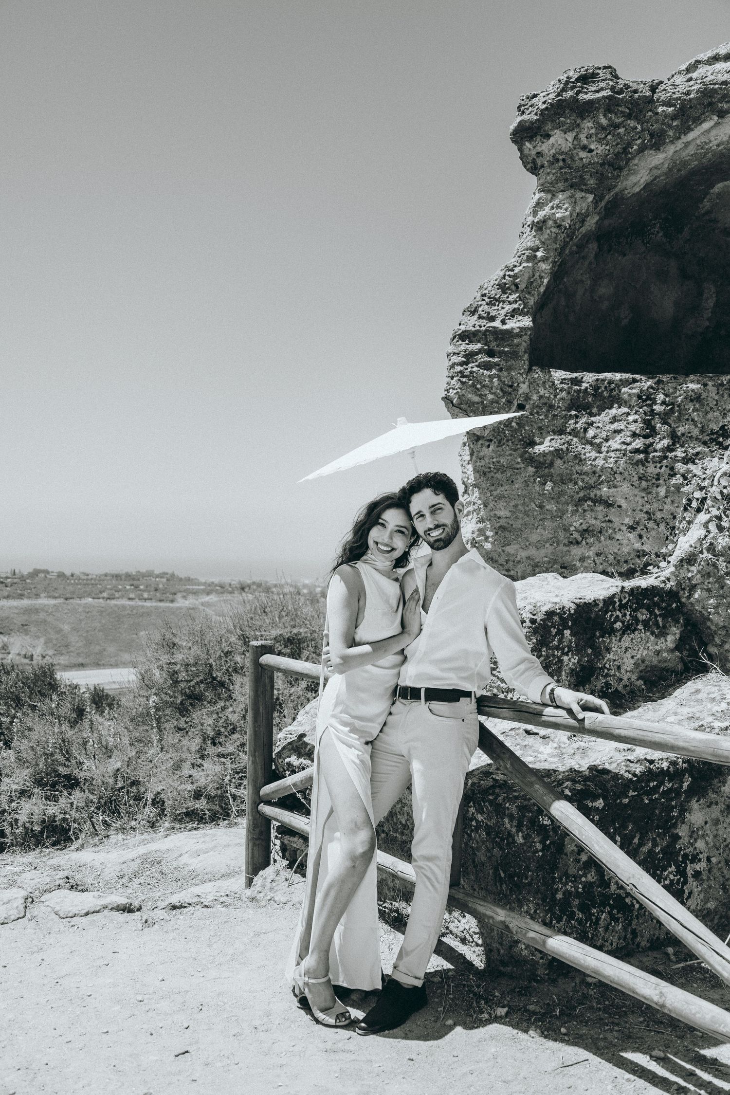 Couple in white outfits pose together against rocky cliffs and scenic overlook.