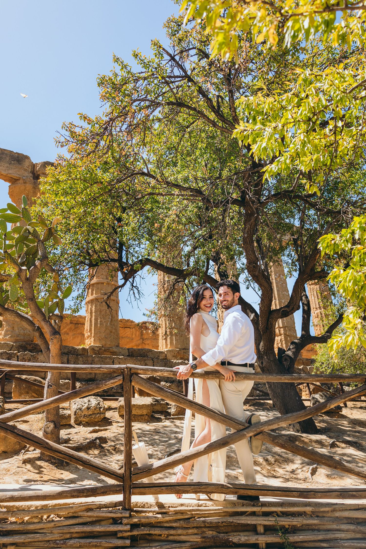 Autumn trees frame couple in white at historic temple ruins during romantic photoshoot.