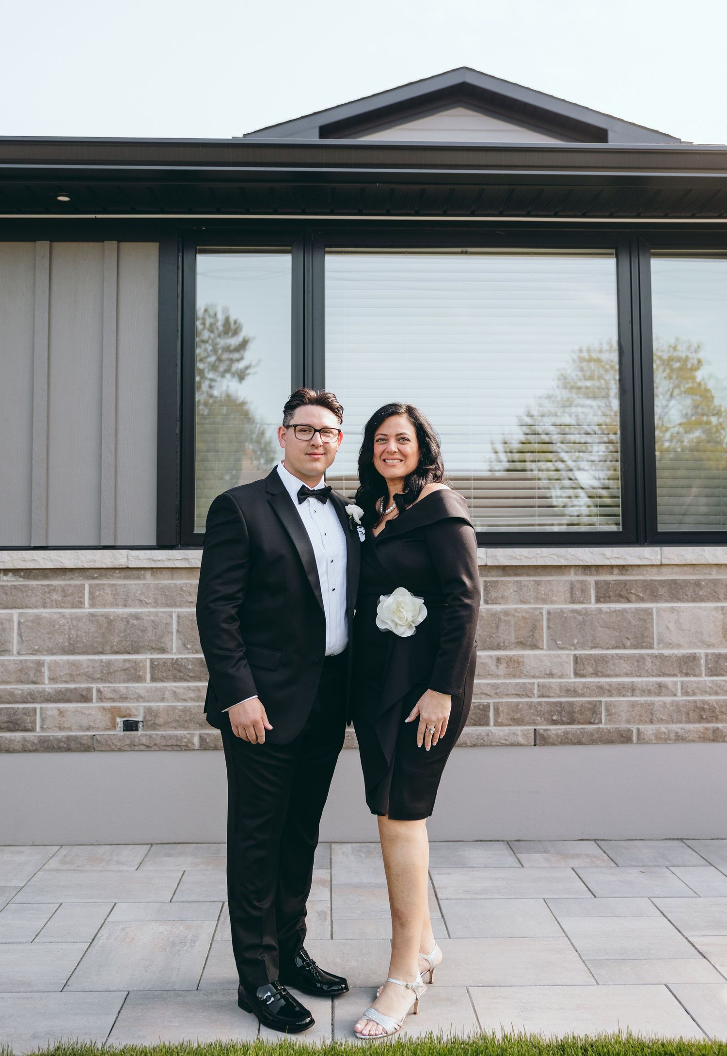 Wedding couple posing casually against modern architecture with stone and glass details.