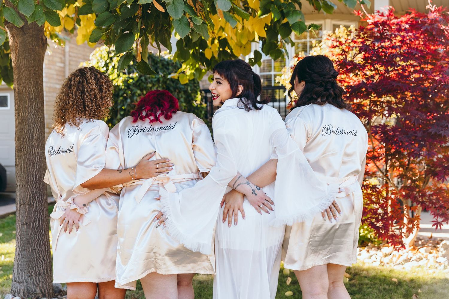 Wedding party wearing matching white robes pose together outdoors.