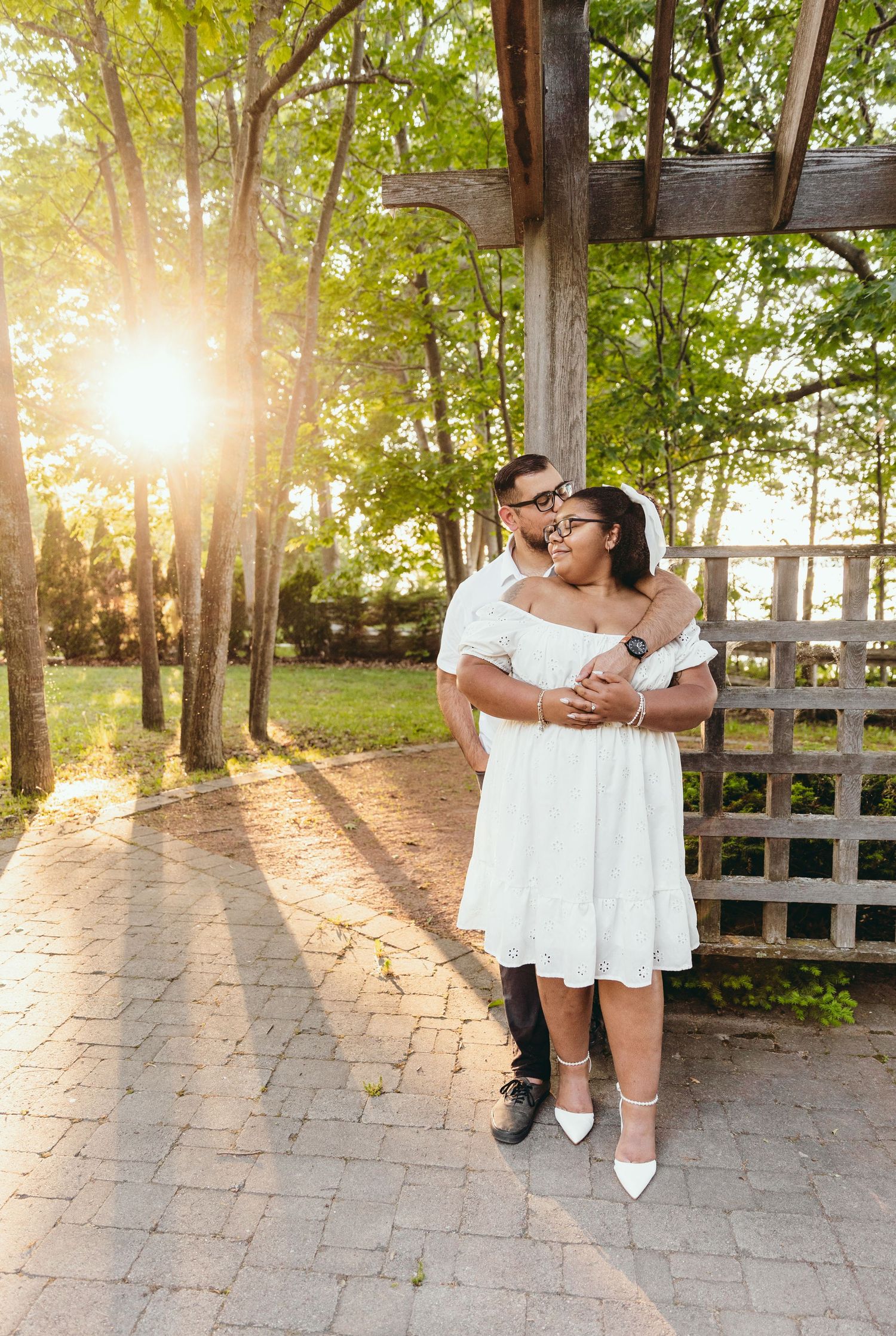 Romantic sunset photoshoot in a park with wooden fencing and golden sunlight streaming through trees.