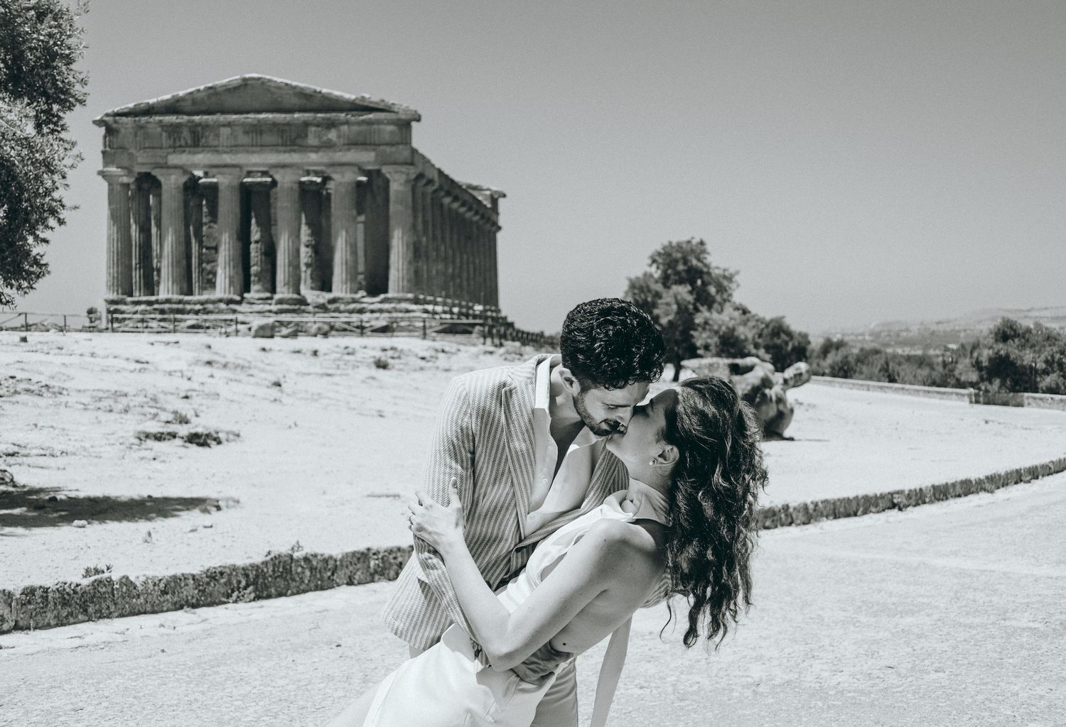 Black and white wedding photos of couple embracing outdoors near stone architecture.