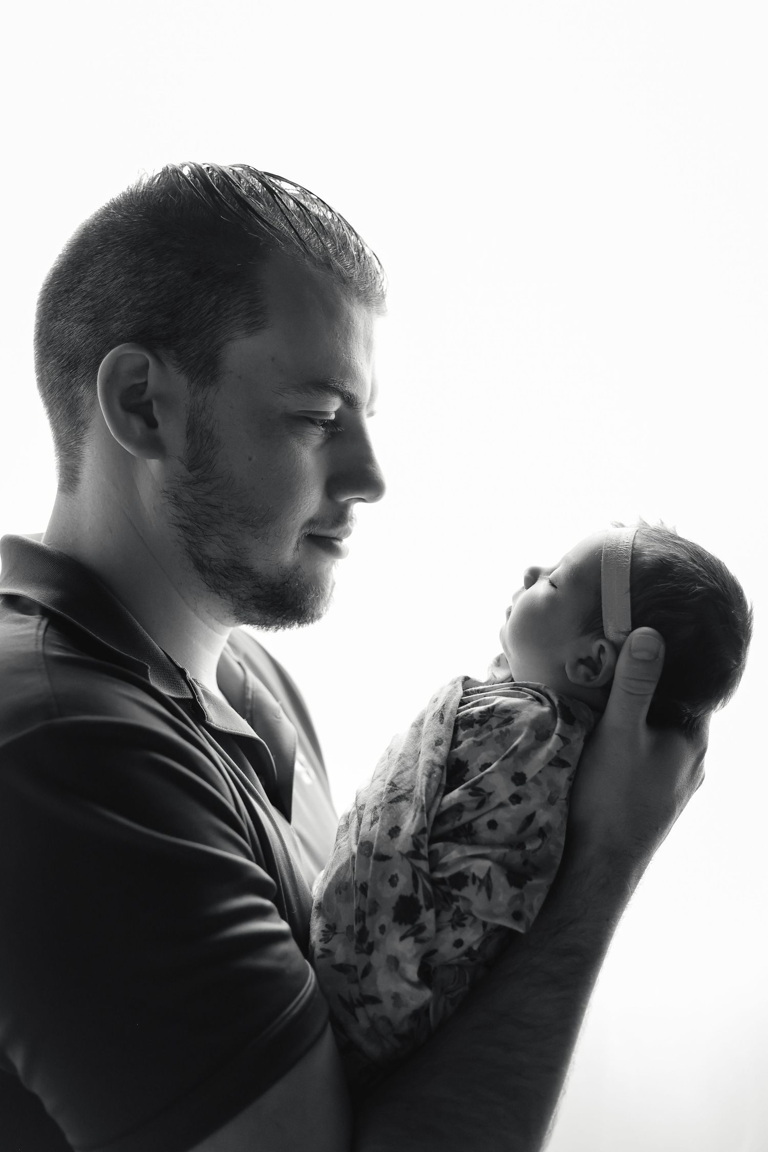Silhouette portrait showing tender moment between parent and newborn in black and white.