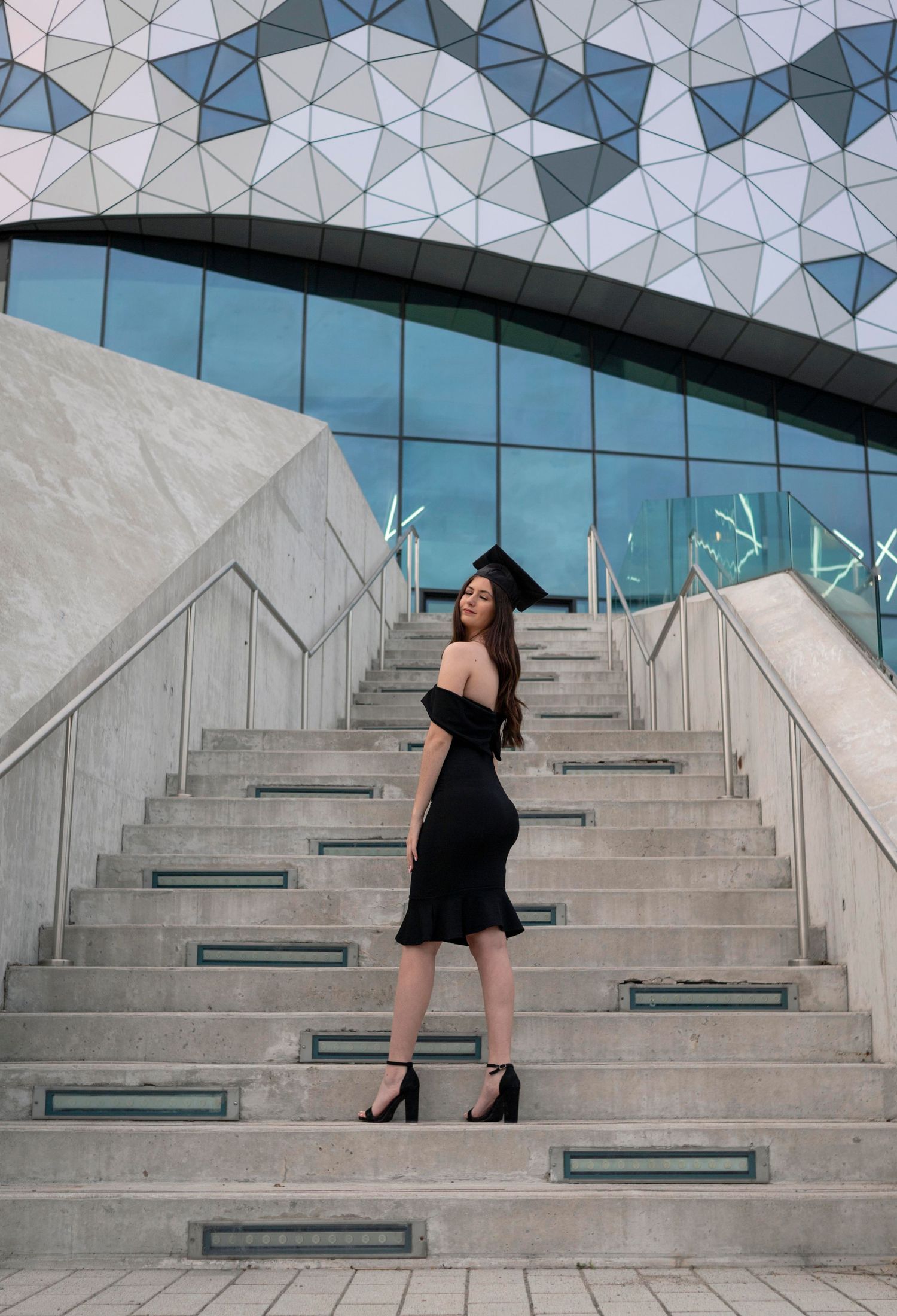 Person in black dress posing on modern geometric stairs with faceted glass wall.