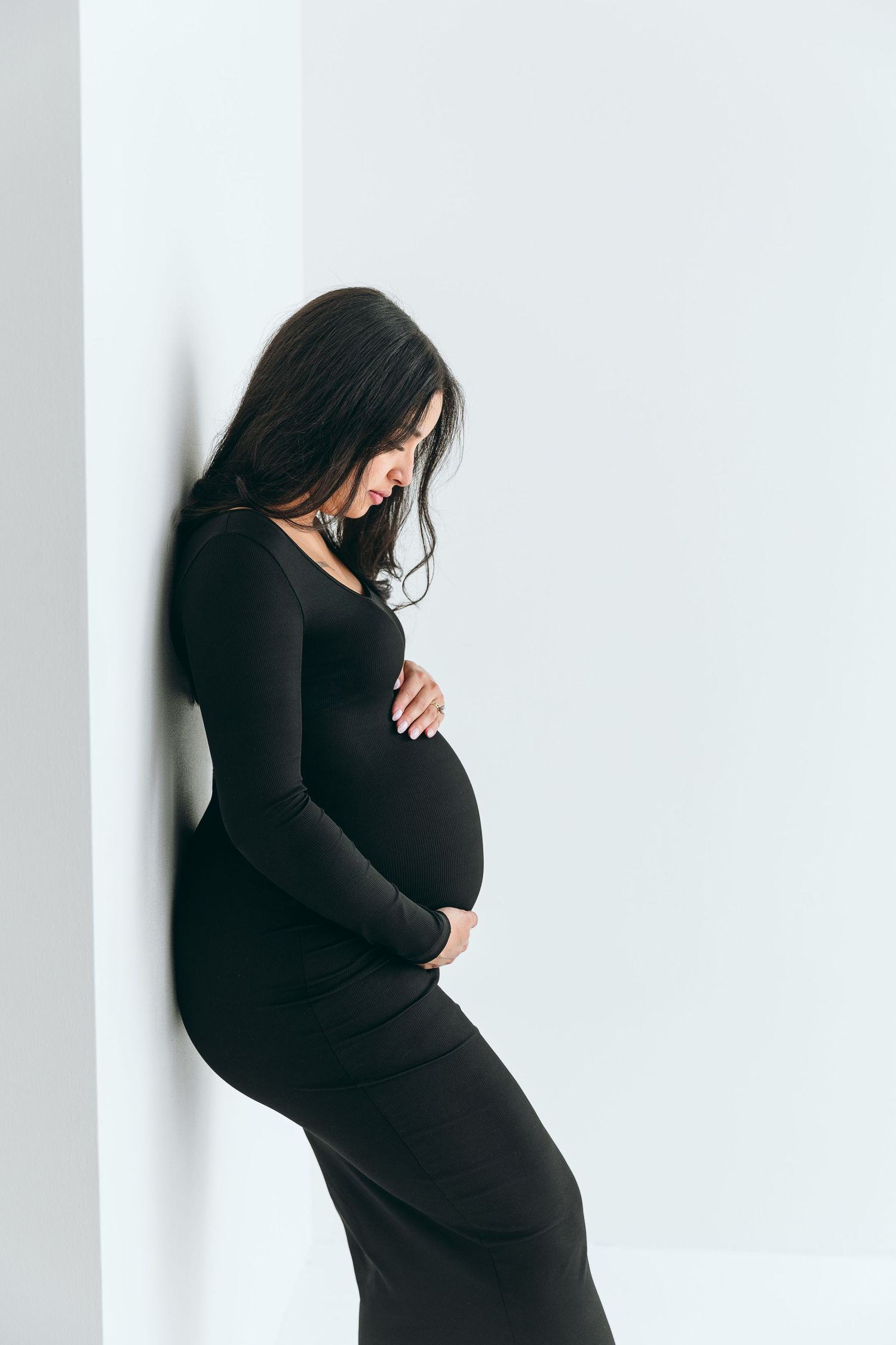 Silhouette of an expectant mother in a black dress against a white wall.