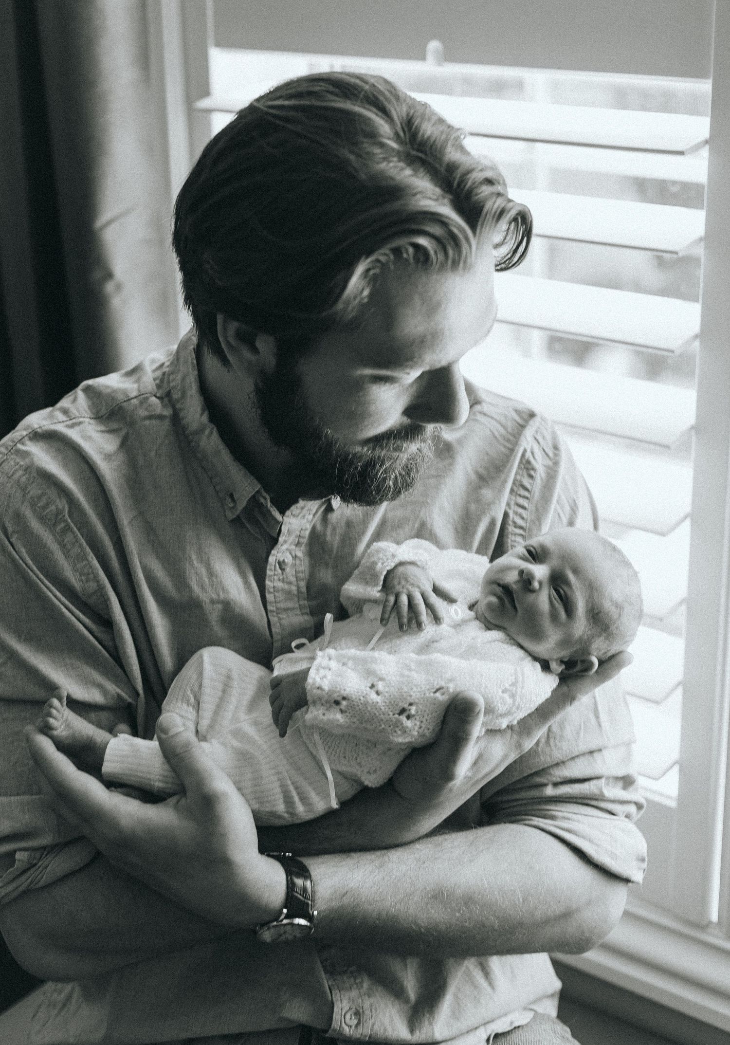 Black and white series of intimate family moments near a window with natural lighting.