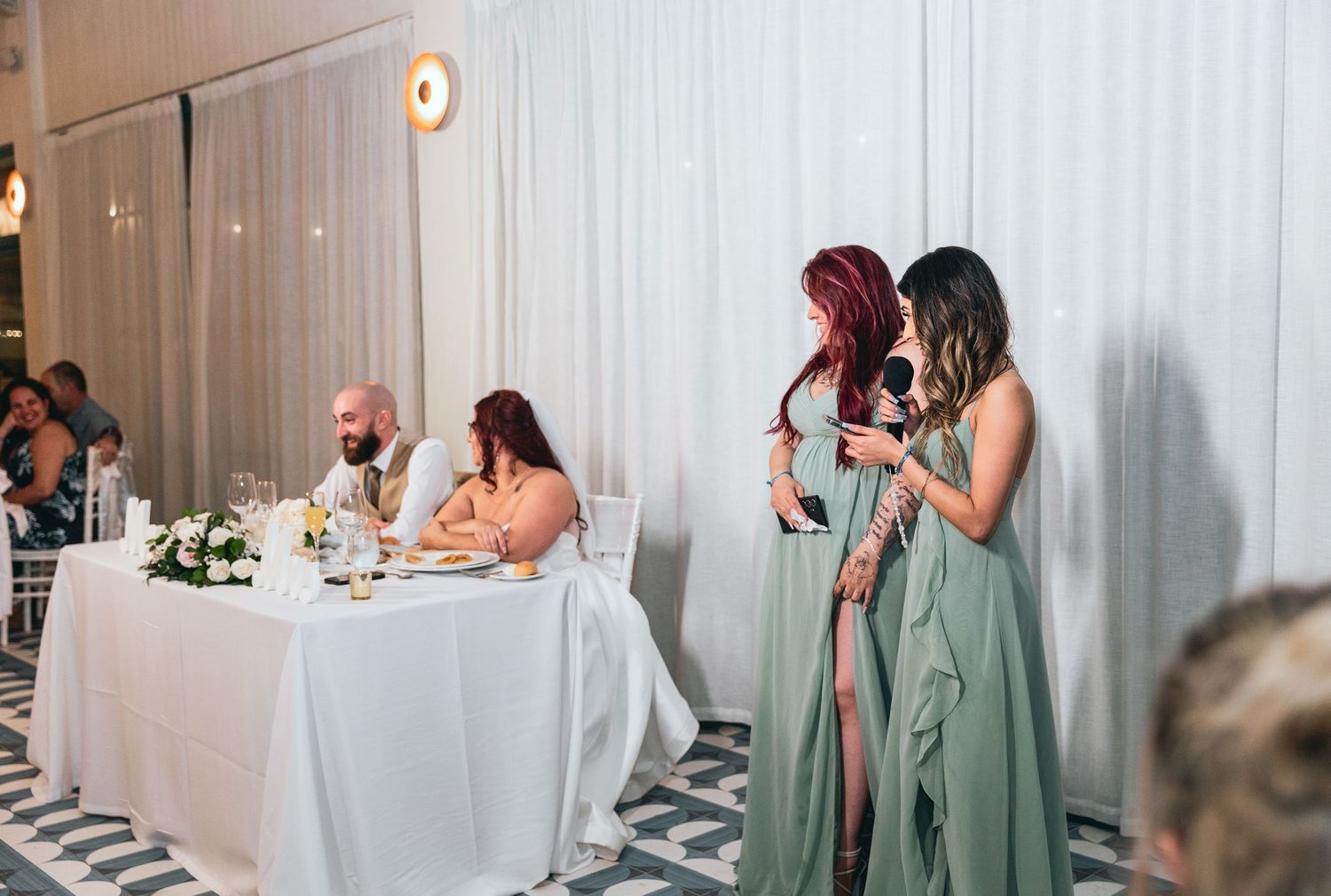Wedding party members in sage green dresses react emotionally during reception speeches.