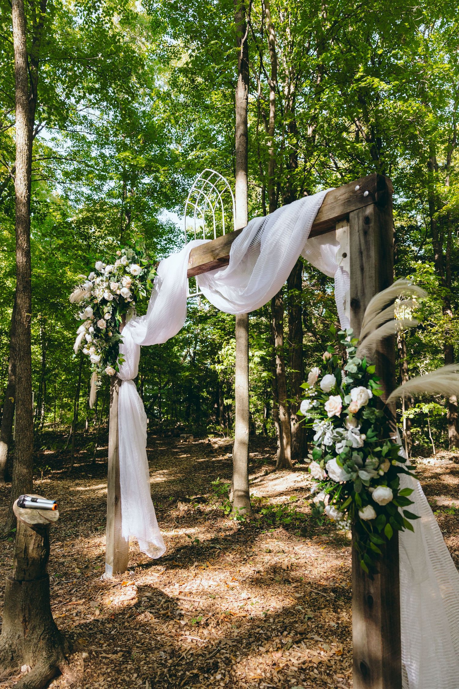 White fabric draping and floral arrangements decorate trees in a forest wedding setting.