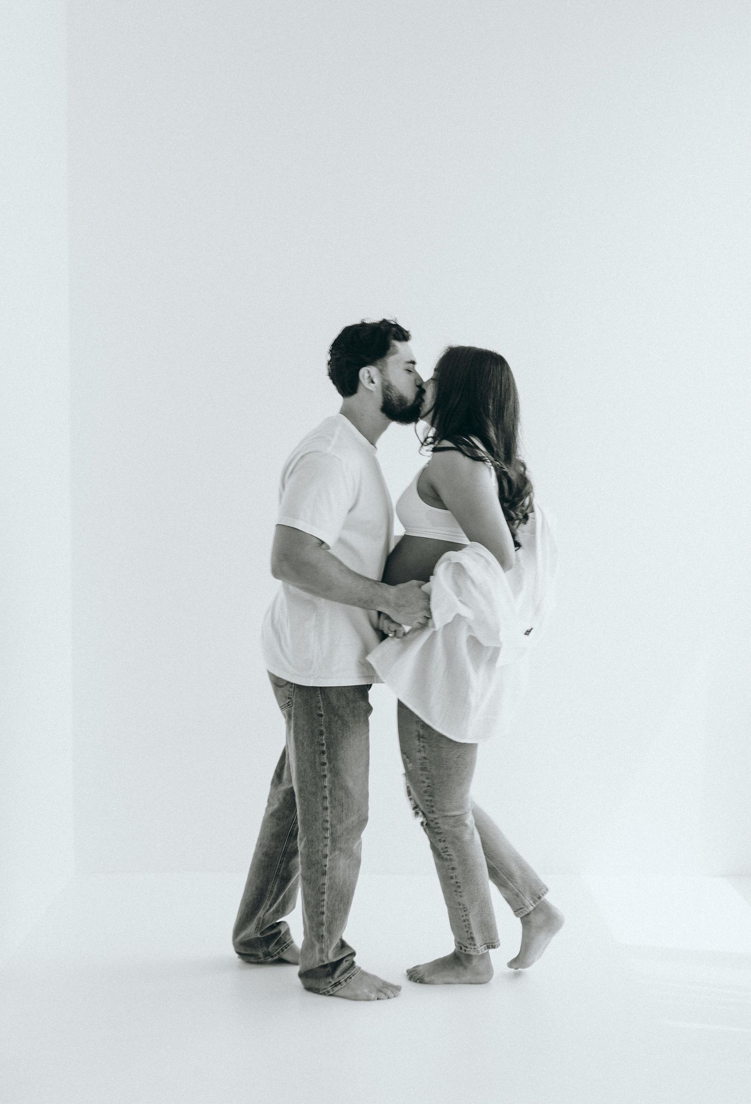 A romantic black and white photo of a couple in casual attire sharing an intimate moment against a white background.