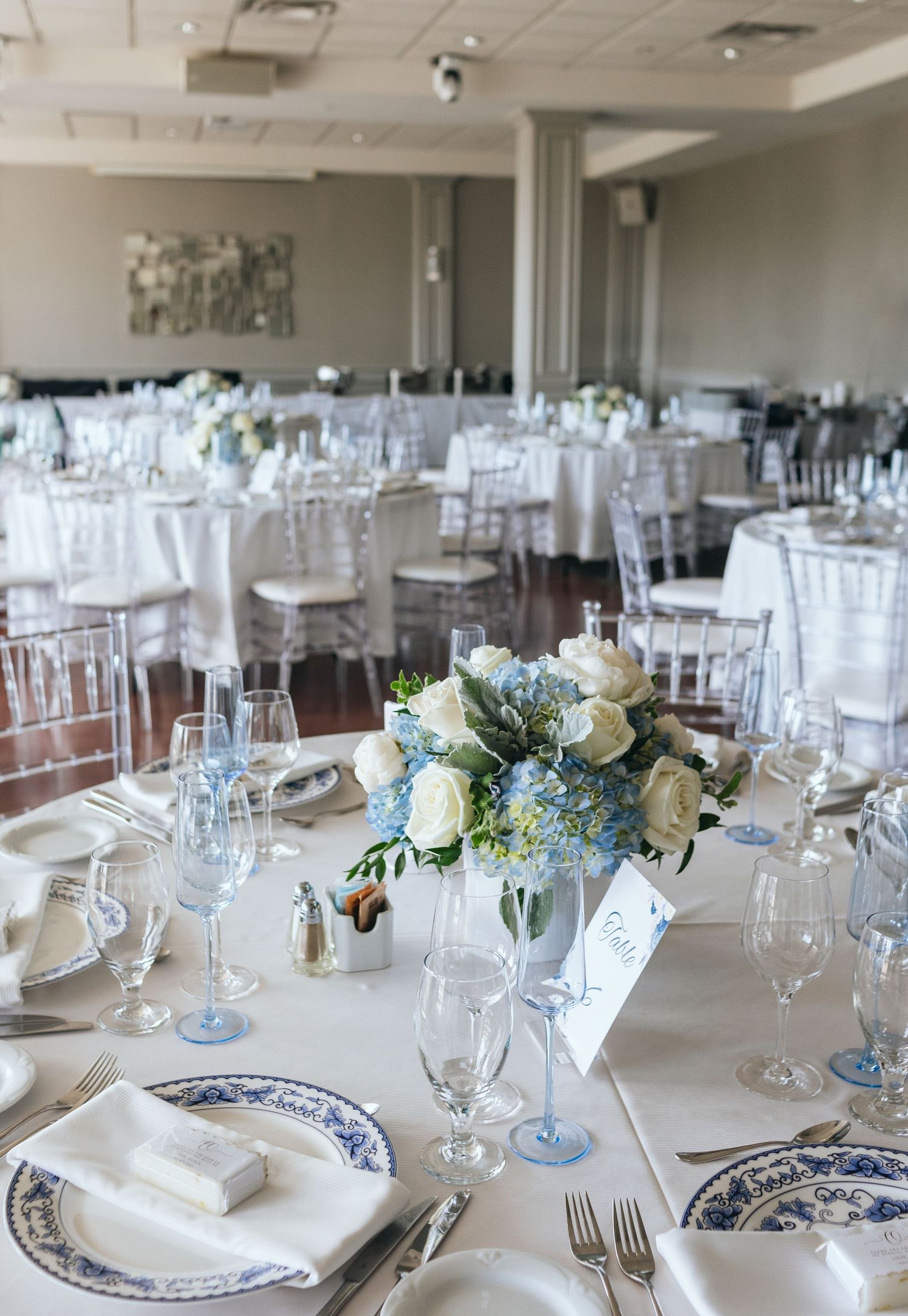 Elegant wedding reception tables set with blue and white china, crystal glasses, and white floral centerpieces.