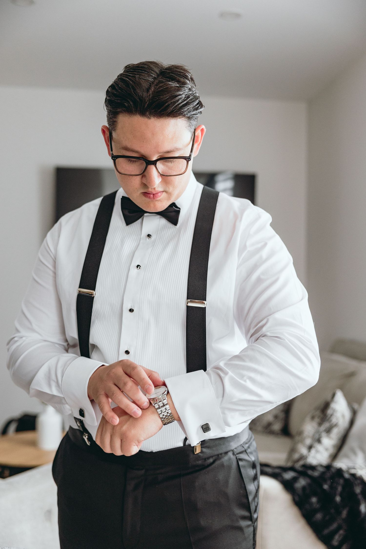 Person in formal white dress shirt and black suspenders adjusting cufflinks while getting ready.