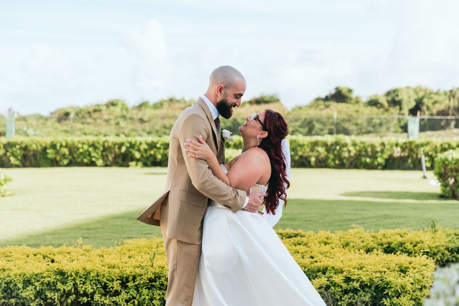 A romantic wedding moment between a couple in formal attire embracing in a garden setting with yellow flowers.