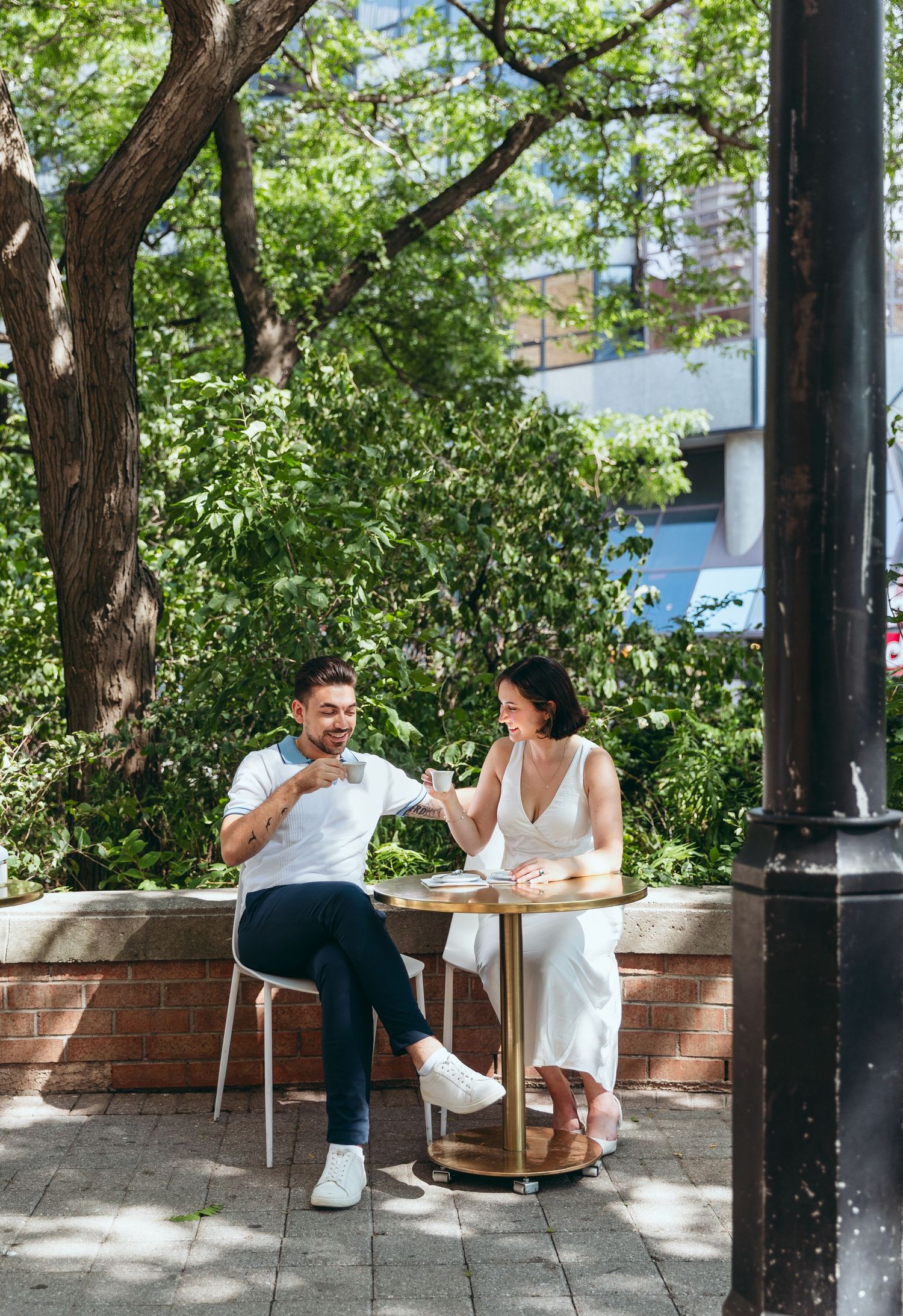 A couple enjoying a casual date at an outdoor plaza surrounded by trees and brick walls.