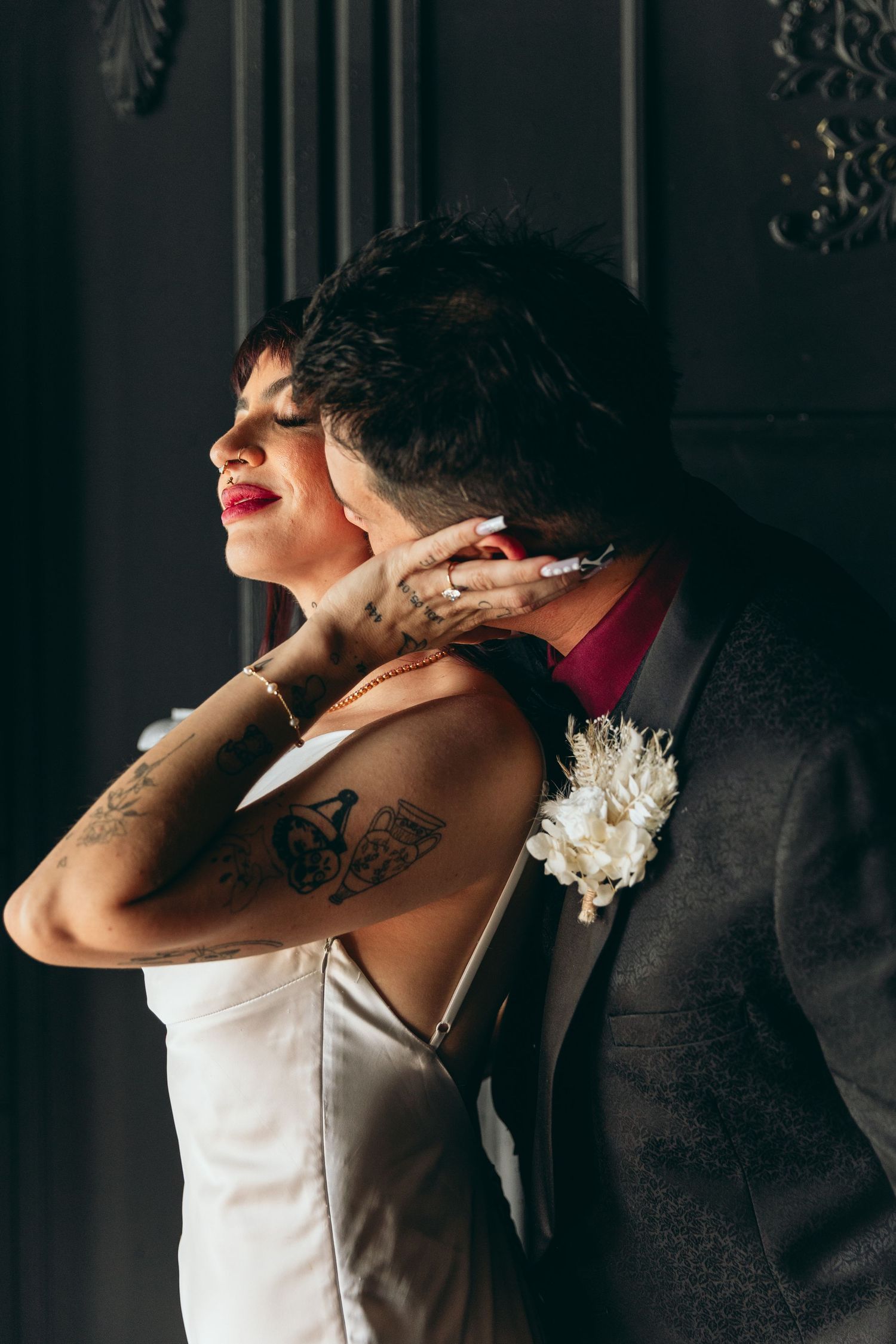An intimate moment between newlyweds in formal attire captured in dramatic lighting.