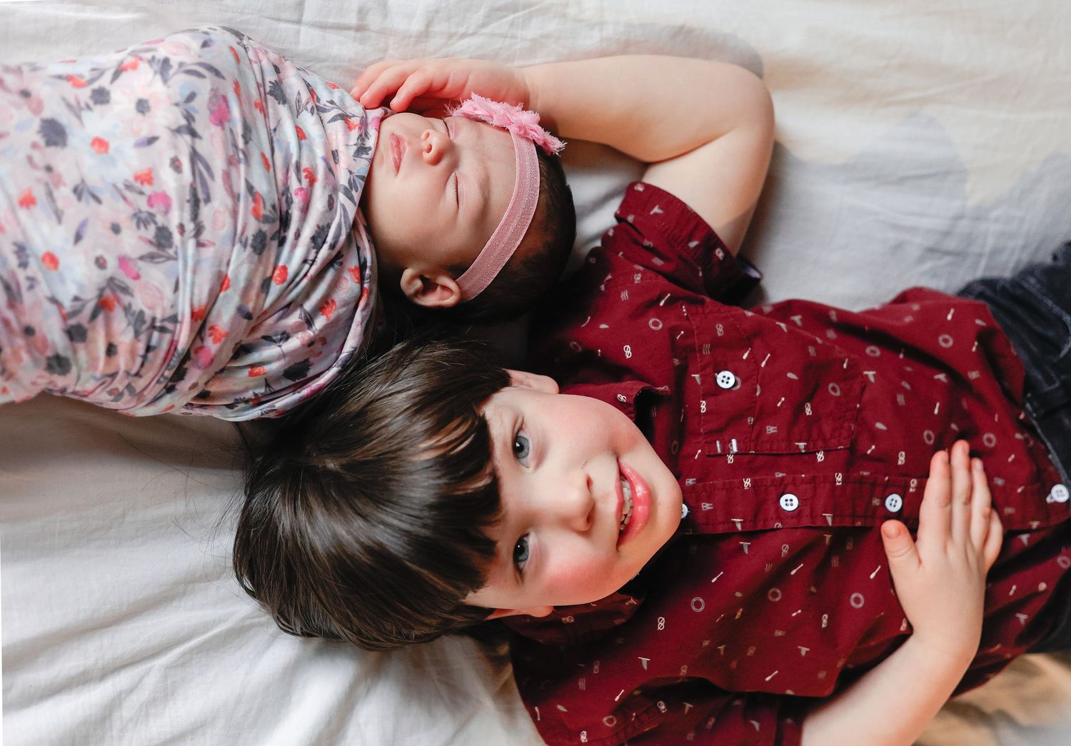 Two children lying on bed wearing festive red and floral outfits.