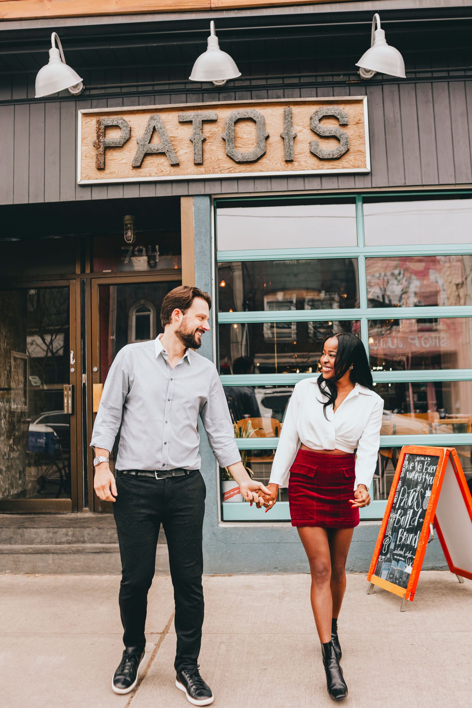 Playful couple walking outside Patois restaurant storefront.