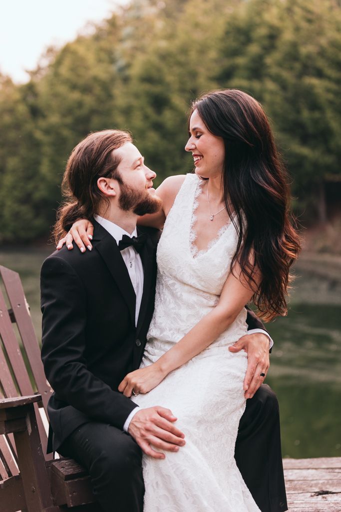 Joyful wedding couple sharing intimate moment on wooden dock by lake.