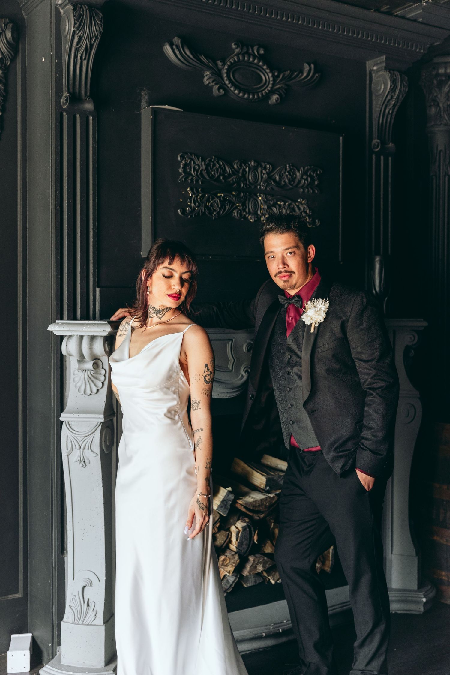 Elegant wedding party poses in formal attire against a dark ornate interior with decorative columns.