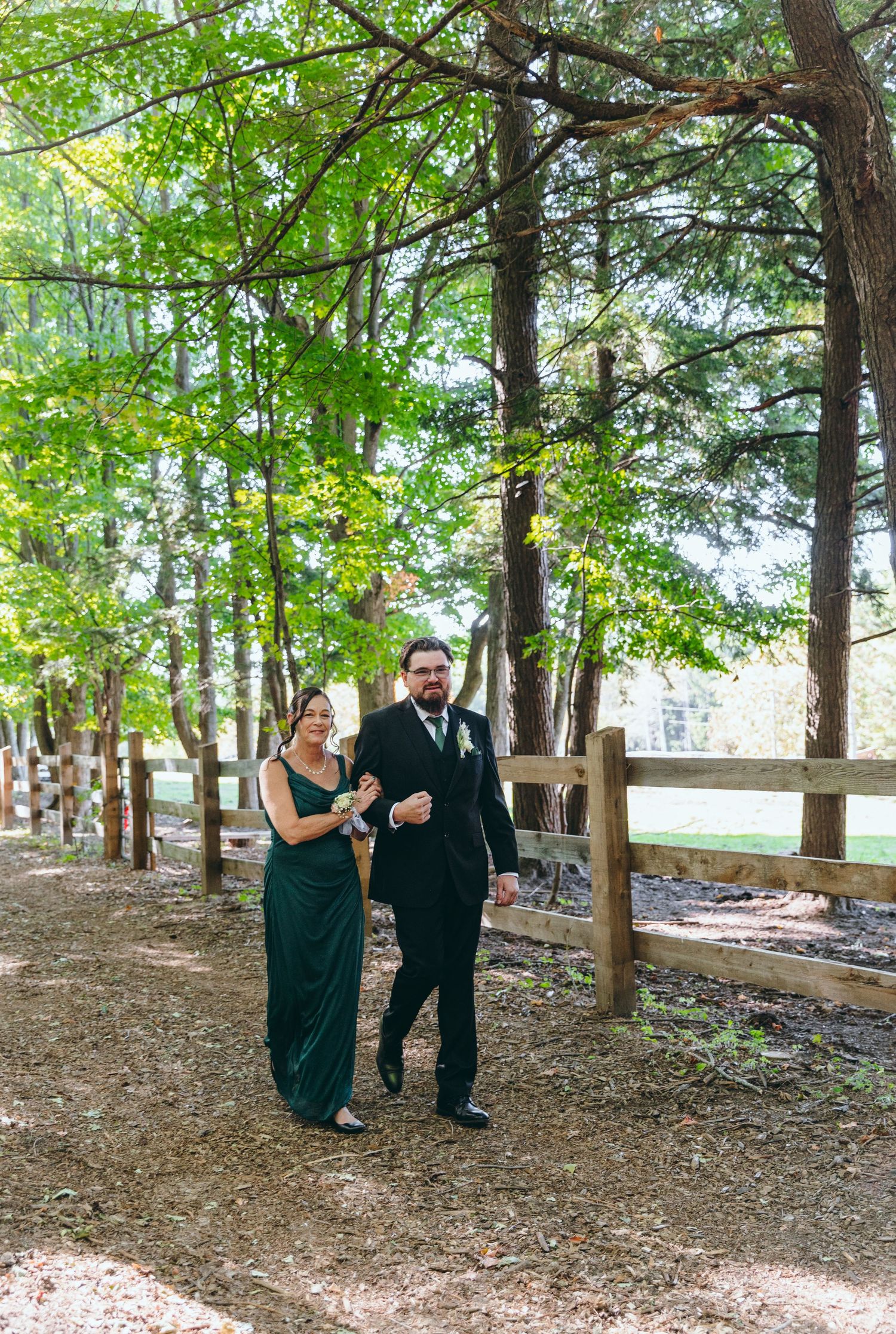 Wedding party members walk through a wooded area in formal attire.