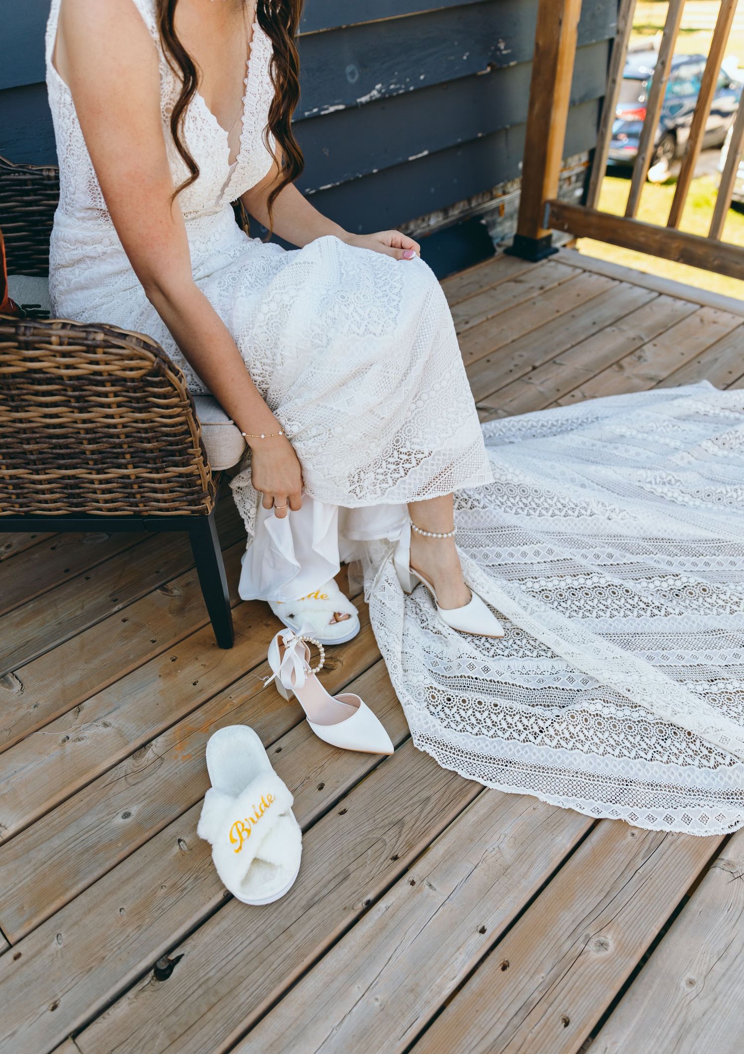 White lace wedding dress and bow shoes arranged on wooden deck planks.