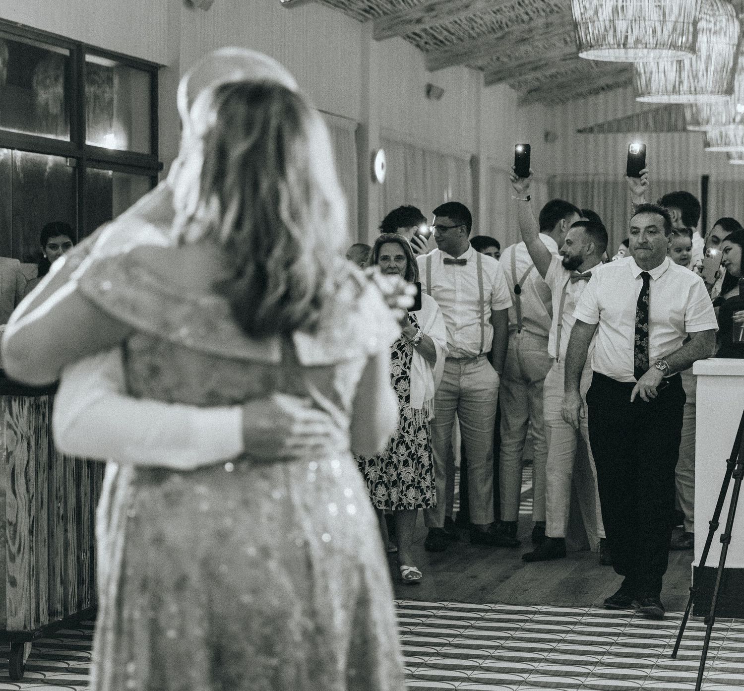 A black and white photo of a couple dancing at a wedding reception with onlookers on a patterned floor.