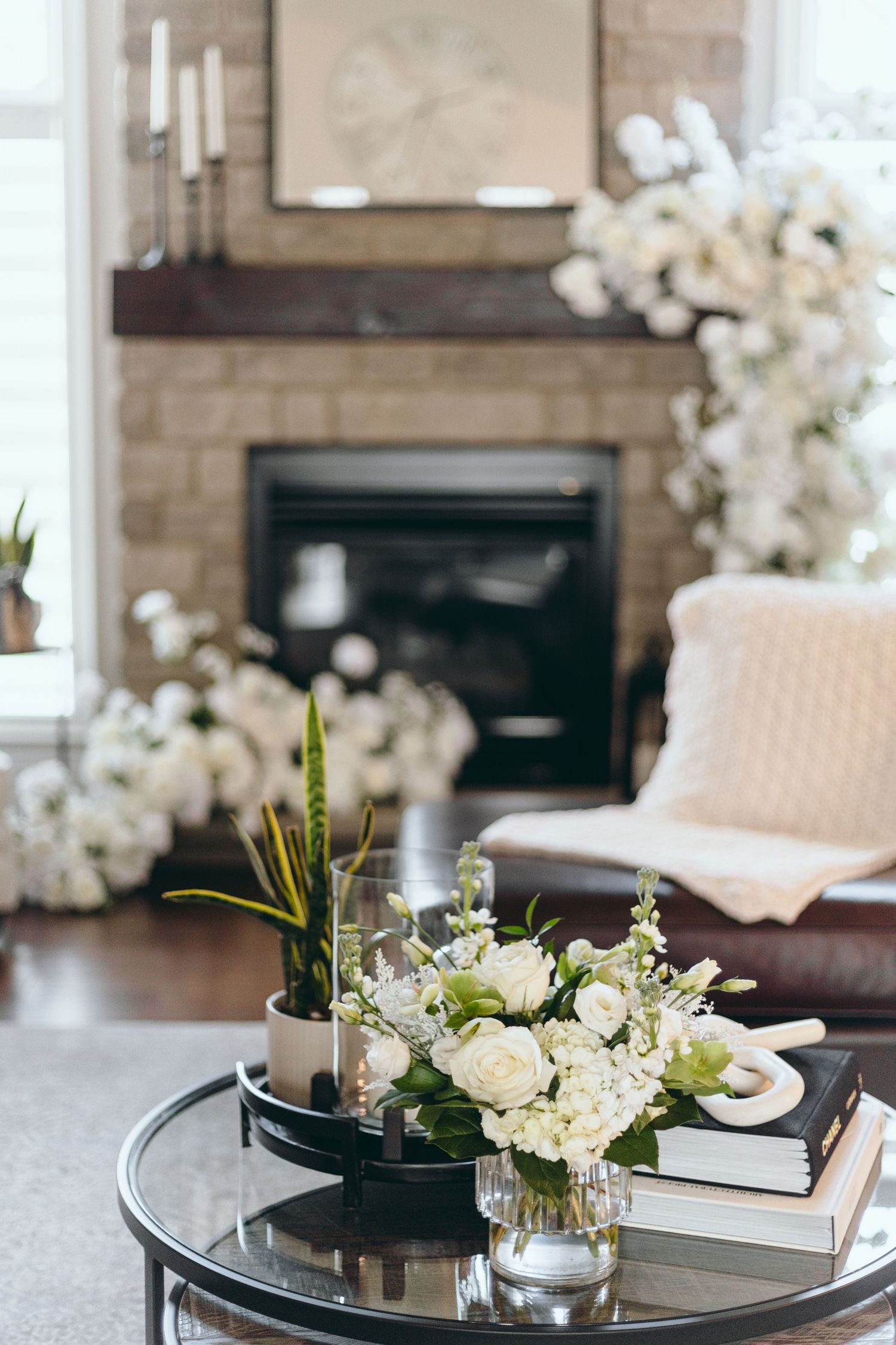 Elegant living room with white floral arrangements and stone fireplace.