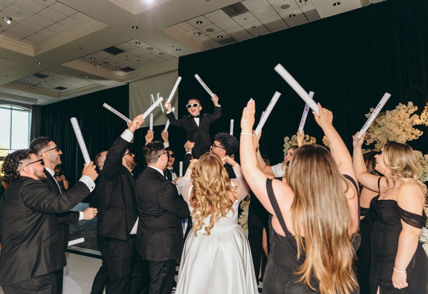 Wedding celebration with guests holding glowing light sticks on the dance floor during reception.