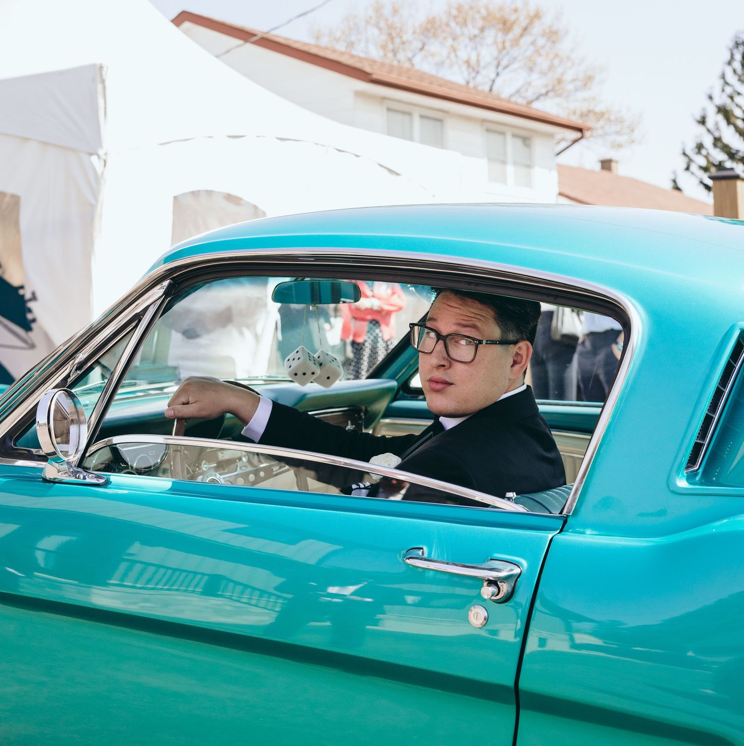 Person in formal attire sits in a turquoise classic car.