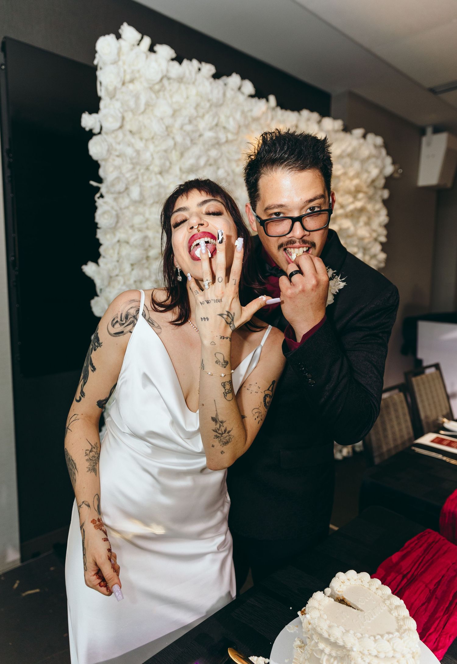 A couple shares a playful moment while cutting their white wedding cake.