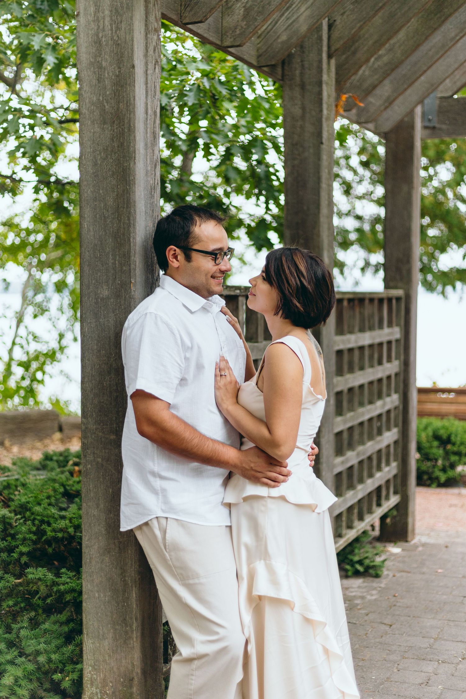 A couple in white outfits sharing an intimate moment under a wooden pergola.